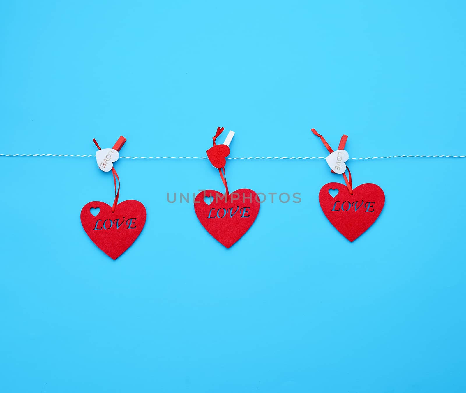 three red felt hearts hanging on a white rope and fastened with a clothespin, blue background. Holiday celebration concept. 