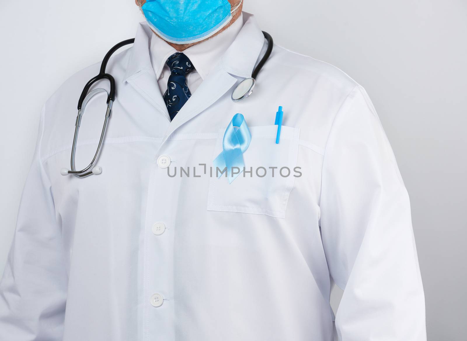 male doctor in a white coat and tie stands. On the pocket pinned a blue ribbon in the shape of a loop, symbol of the fight and treatment of prostate cancer