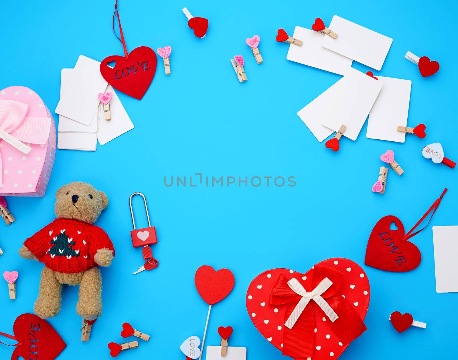 cardboard boxes in the form of a heart, a small teddy bear, white blank business cards with clothespins on a blue background, decor and objects for Valentine's Day, flat lay, copy space