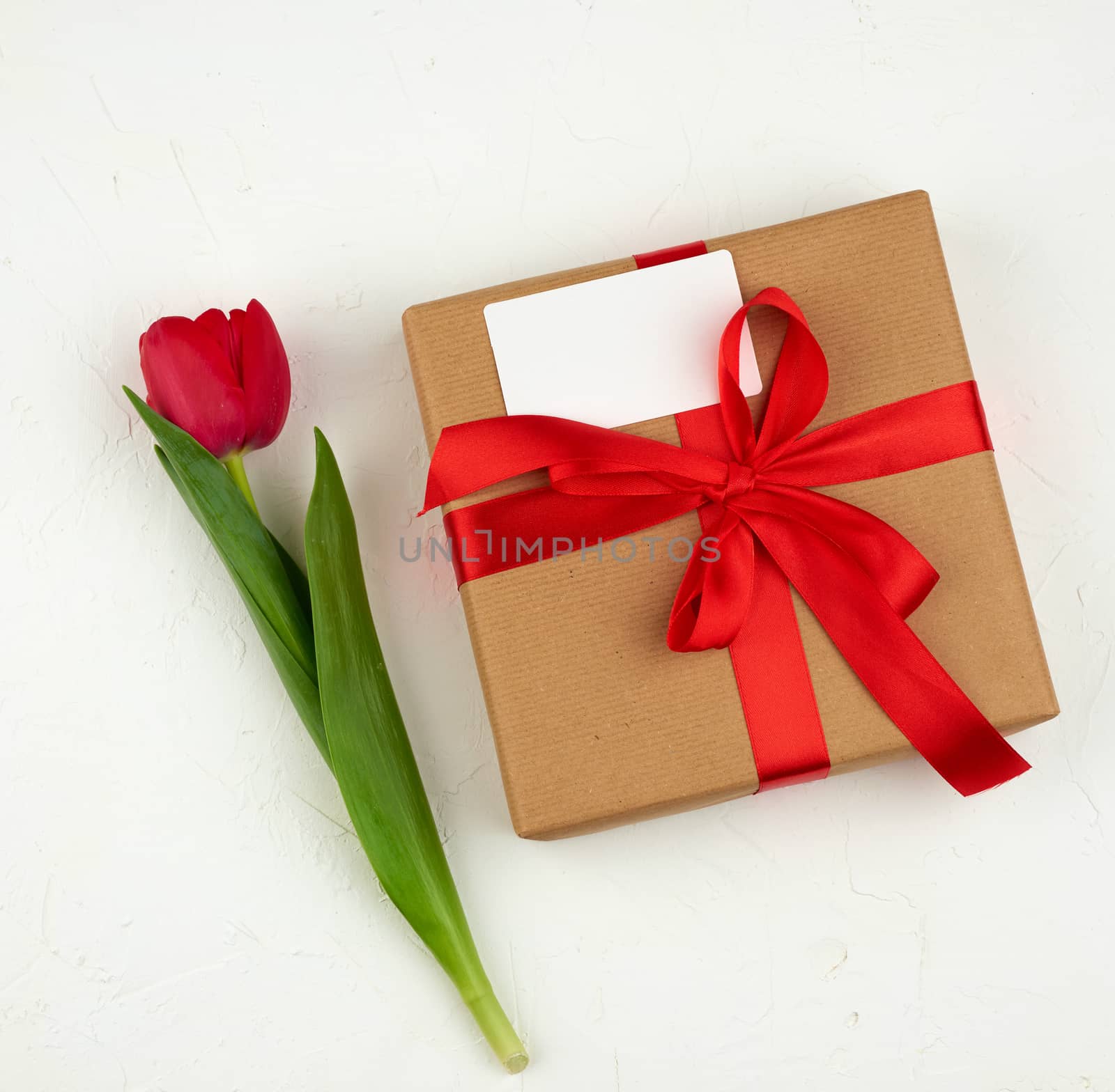 bouquet of red blooming tulips with green leaves, wrapped gift in brown craft paper on a white background. Festive backdrop for birthday, Valentine's day