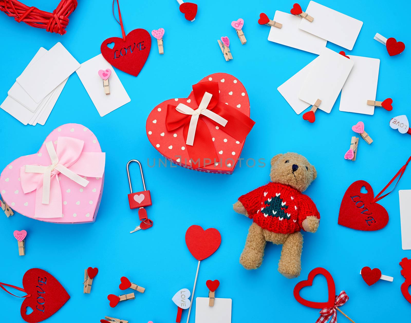 cardboard boxes in the form of a heart, a small teddy bear, white blank business cards with clothespins on a blue background, decor and objects for Valentine's Day, flat lay