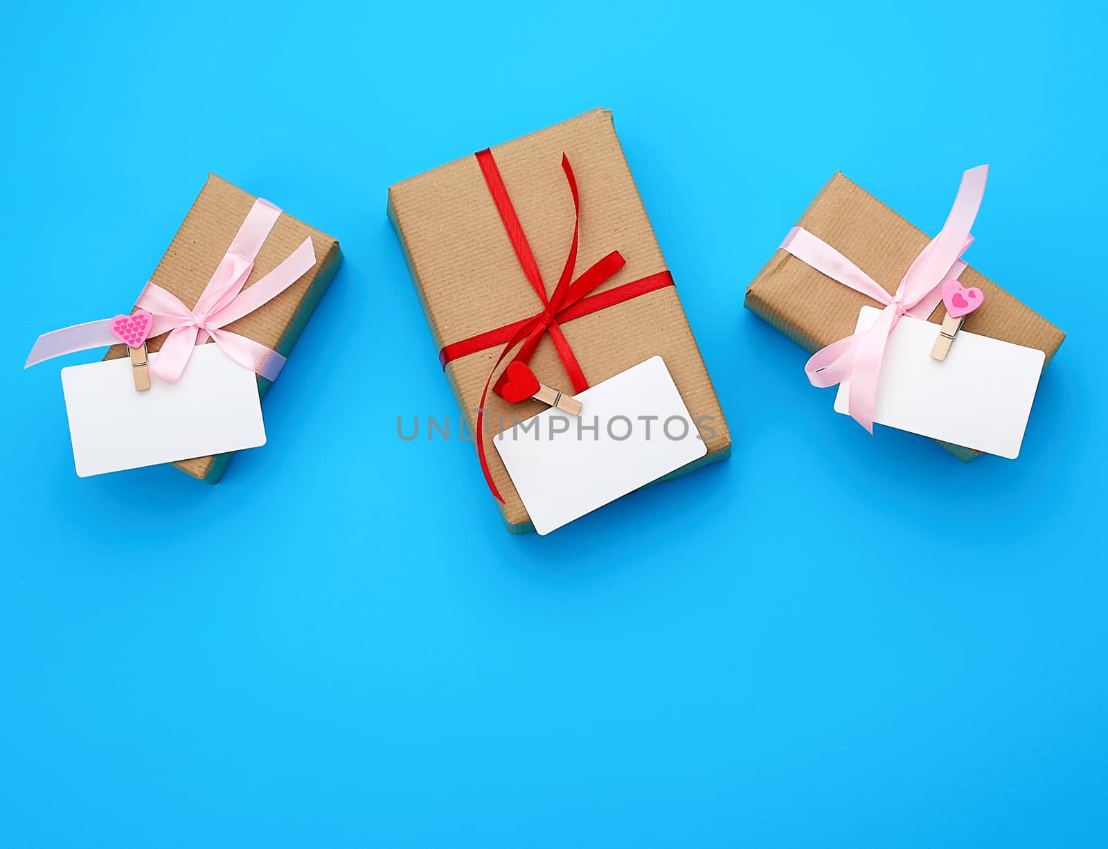 box is wrapped in brown paper and tied with a red thin silk ribbon on a blue background, copy space, holiday is Valentine's Day