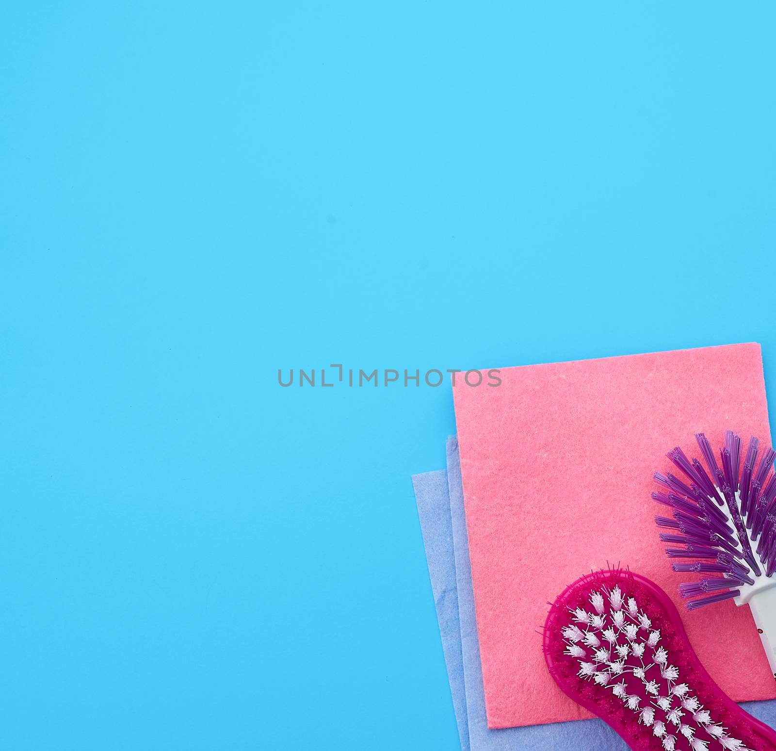 plastic pink brush and square dishwashing sponges on a blue background, top view, flat lay, copy space