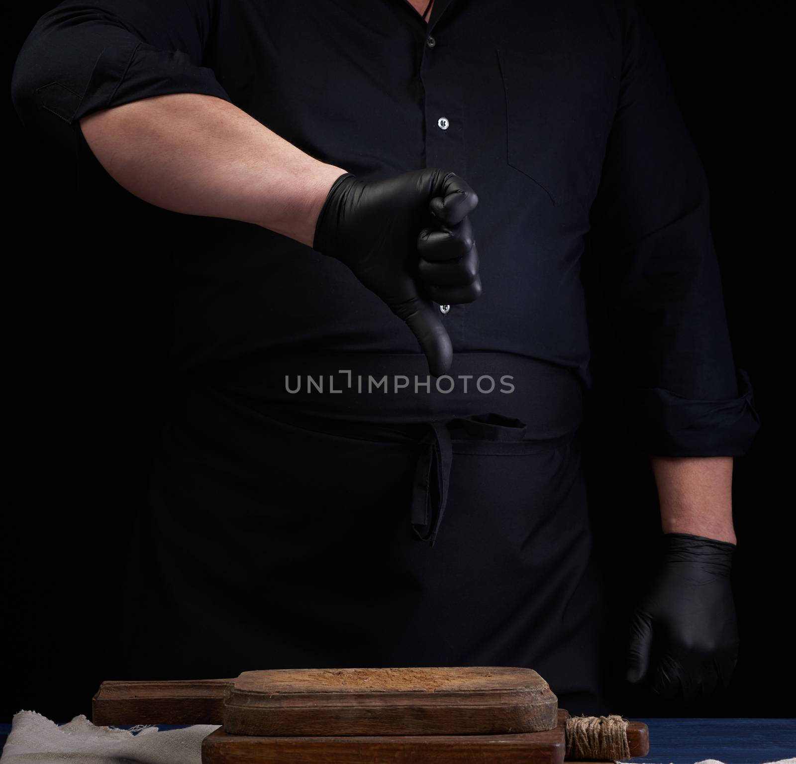 chef in black latex gloves and a black uniform shows with his right hand a gesture of dislike, low key