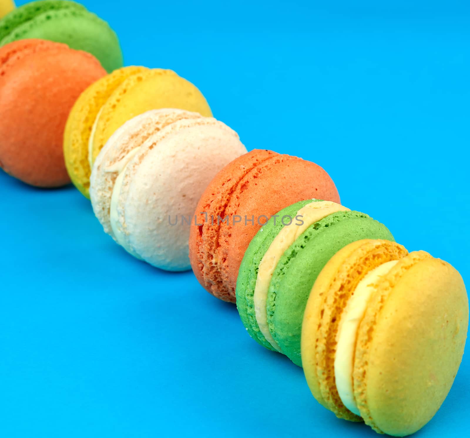round multi-colored baked macarons with cream lie in a line on a blue background, close up