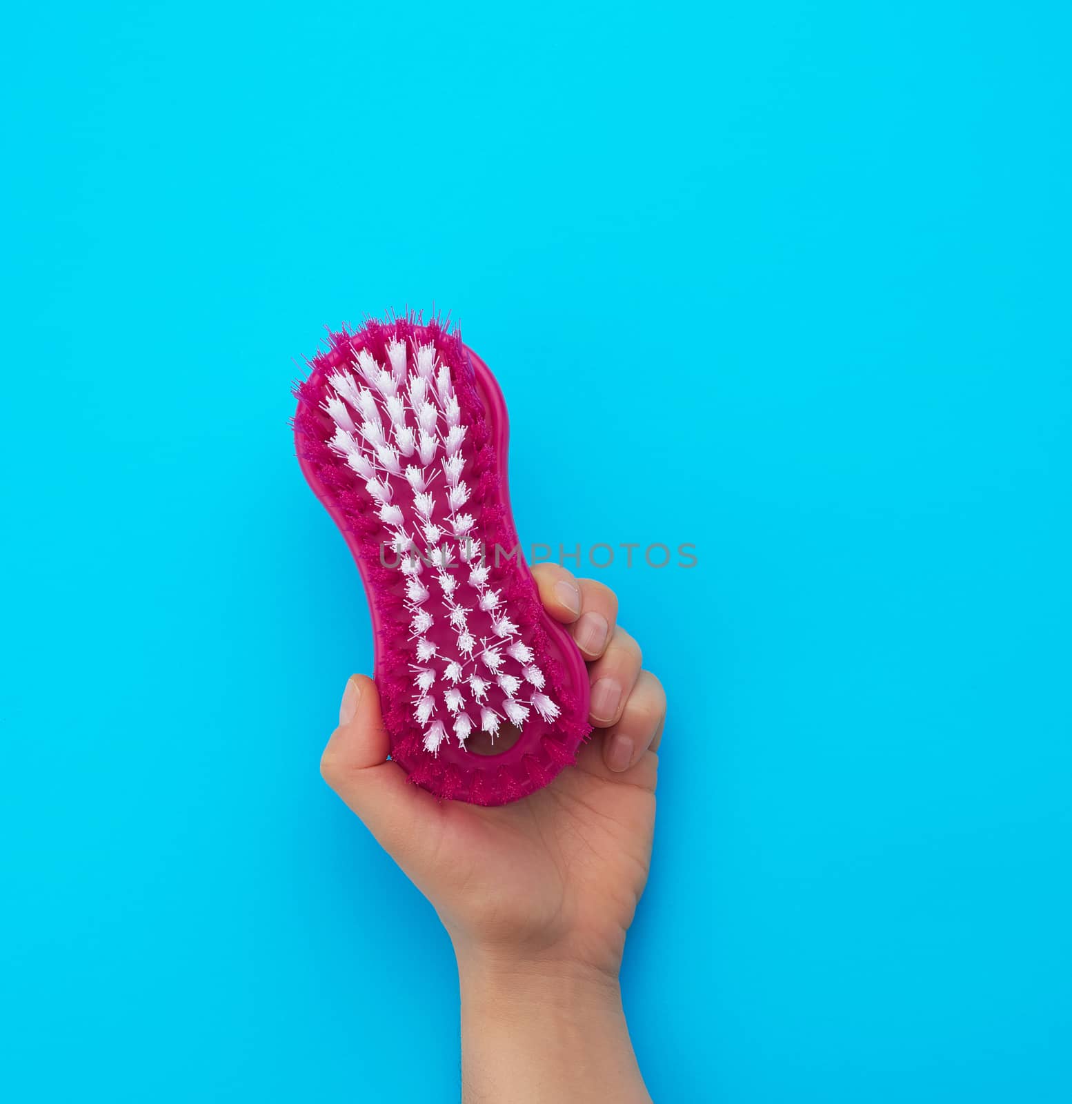 hand holds a plastic brush for cleaning housework, blue background, close up