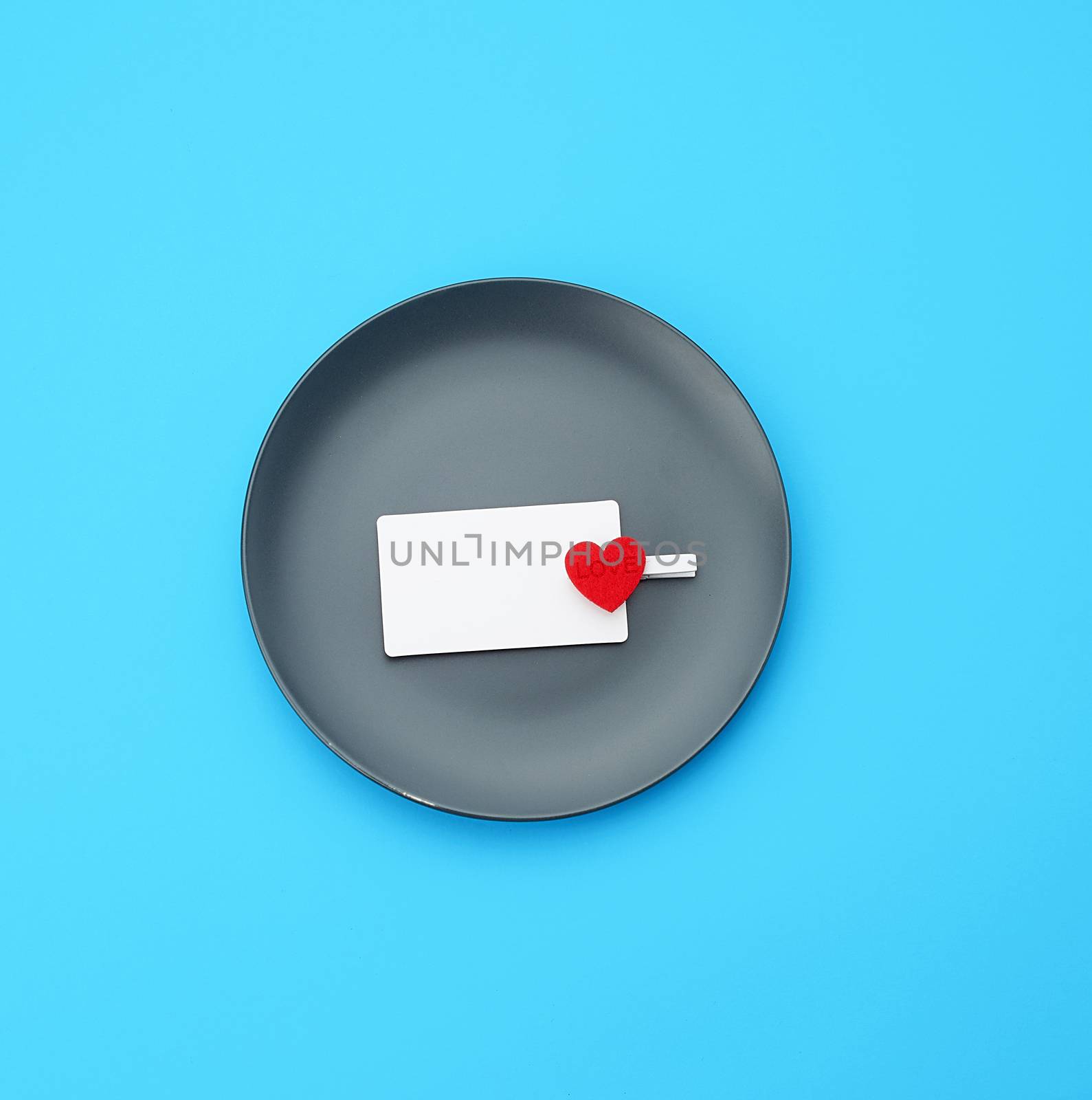 empty round gray plate and decorative red heart, next to an empty white business card, blue background