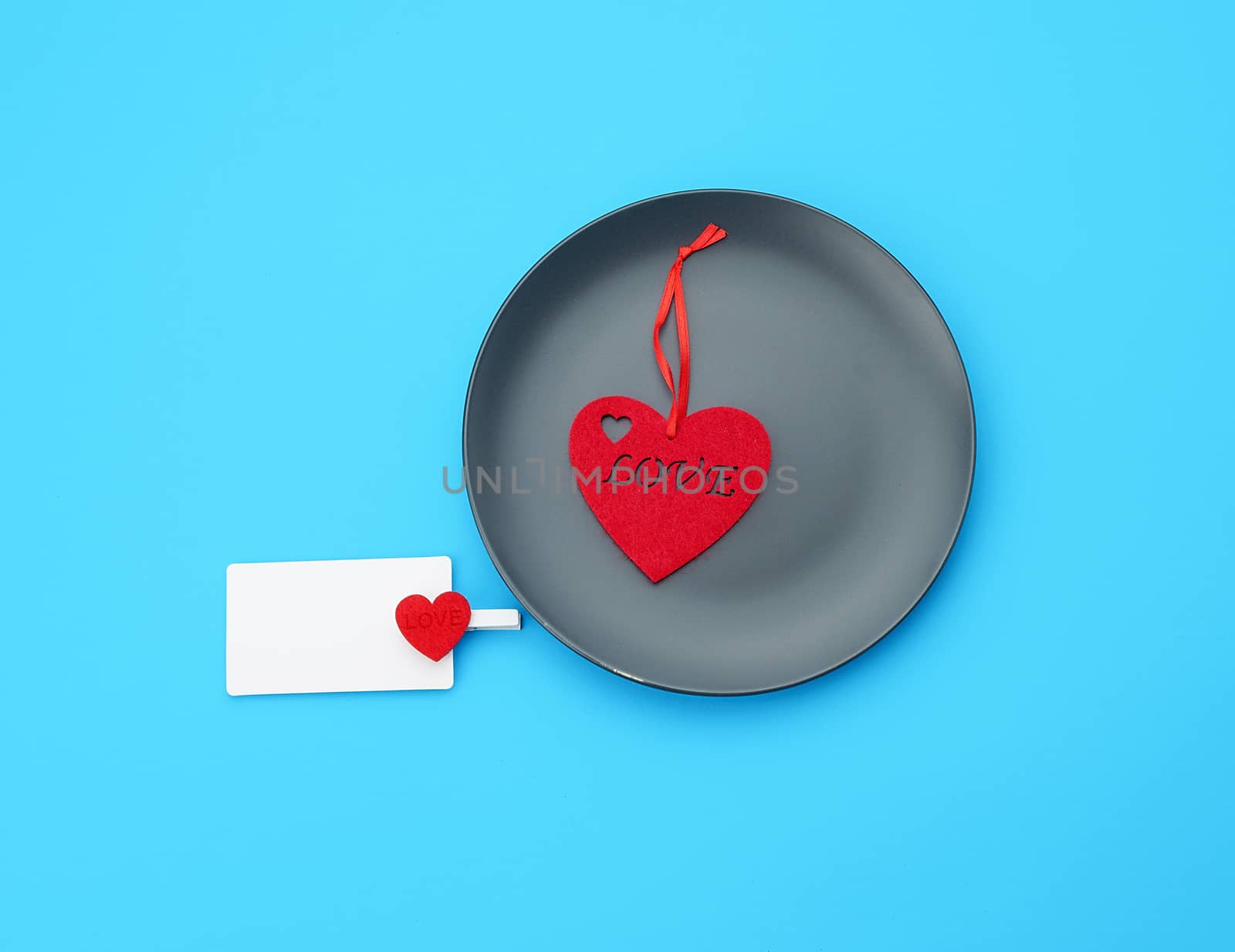empty round gray plate and decorative red heart, next to an empty white business card, blue background