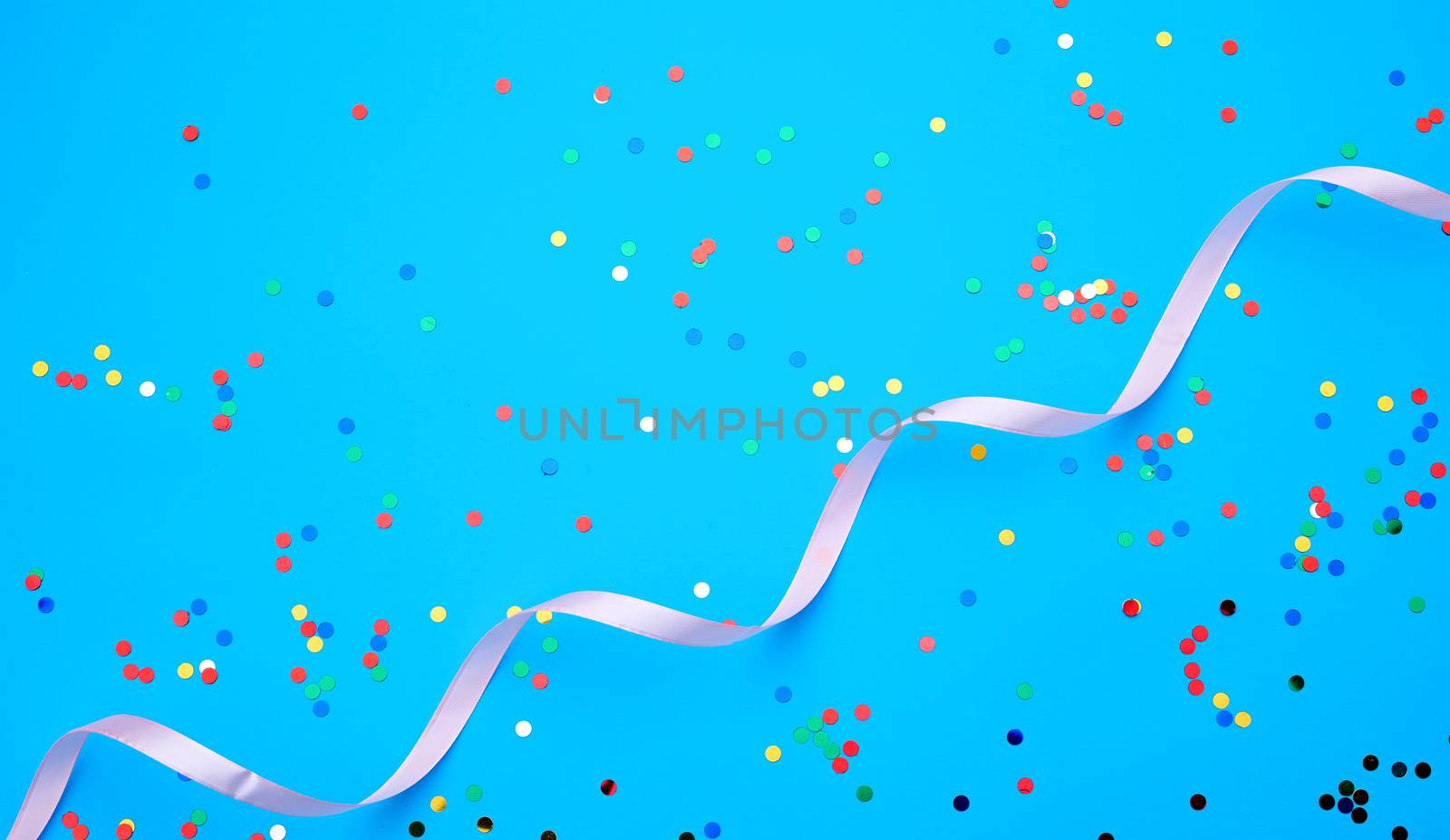 shiny multicolored round confetti scattered on a blue background and pink ribbon, festive backdrop for birthday, valentines day