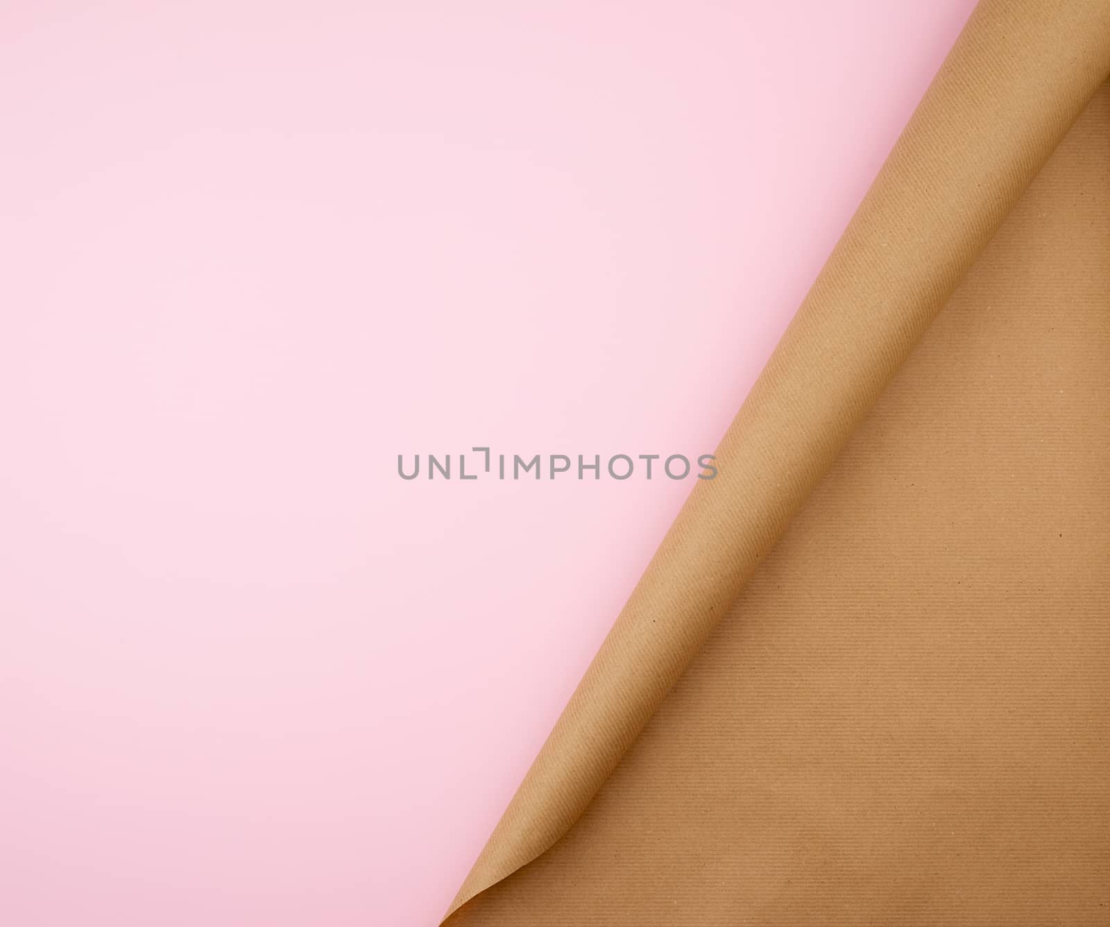 untwisted roll of brown craft paper on a pink background, empty space. Old craft paper texture. Clean sheet, template, angle is twisted