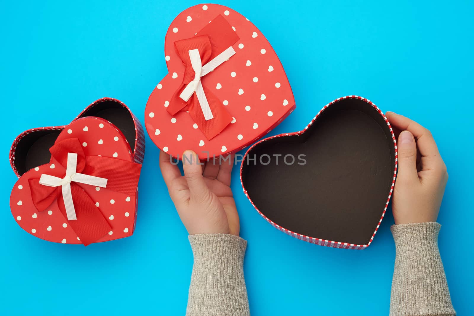 two female hands holding a red cardboard box with a bow on a blue background, concept of giving a gift for a holiday