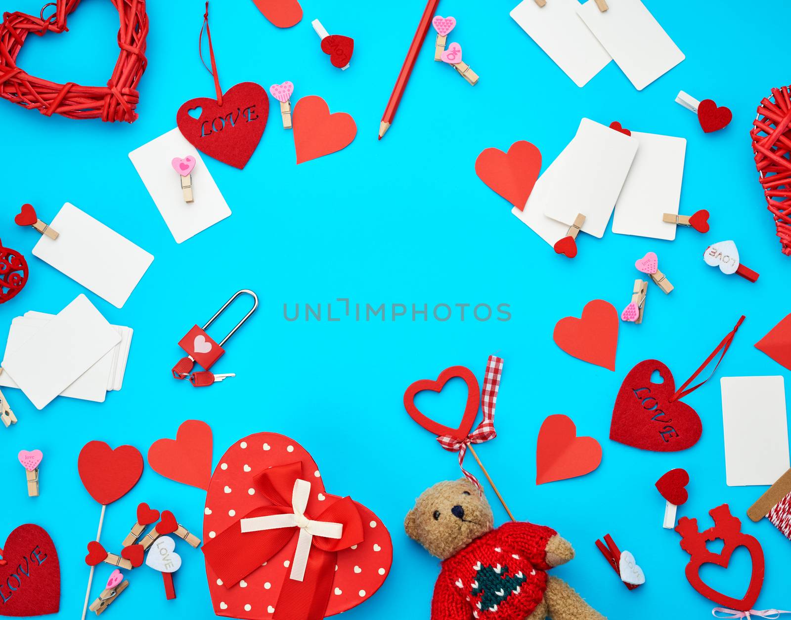 cardboard boxes in the form of a heart, a small teddy bear, white blank business cards with clothespins on a blue background, decor and objects for Valentine's Day, flat lay, copy space