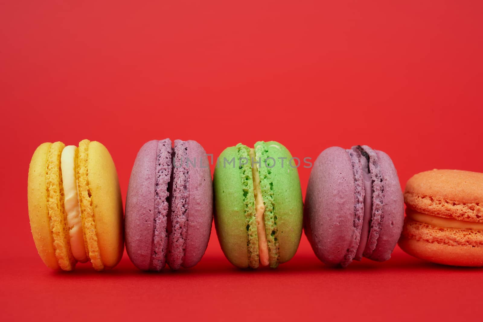 yellow, purple, green round baked macarons cakes on a red background, dessert lies in a row, close up