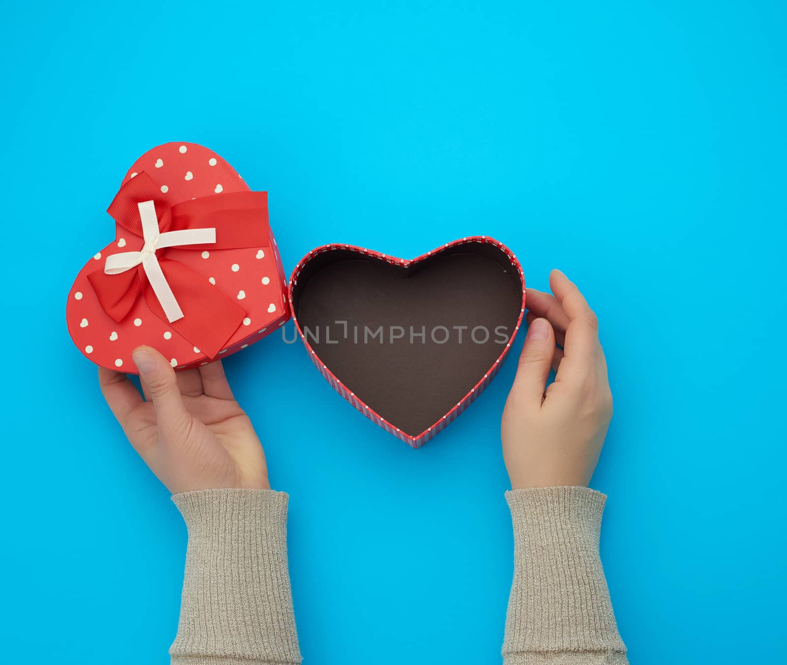 female hand holding a red cardboard box with a bow on a blue background, concept of giving a gift for a holiday