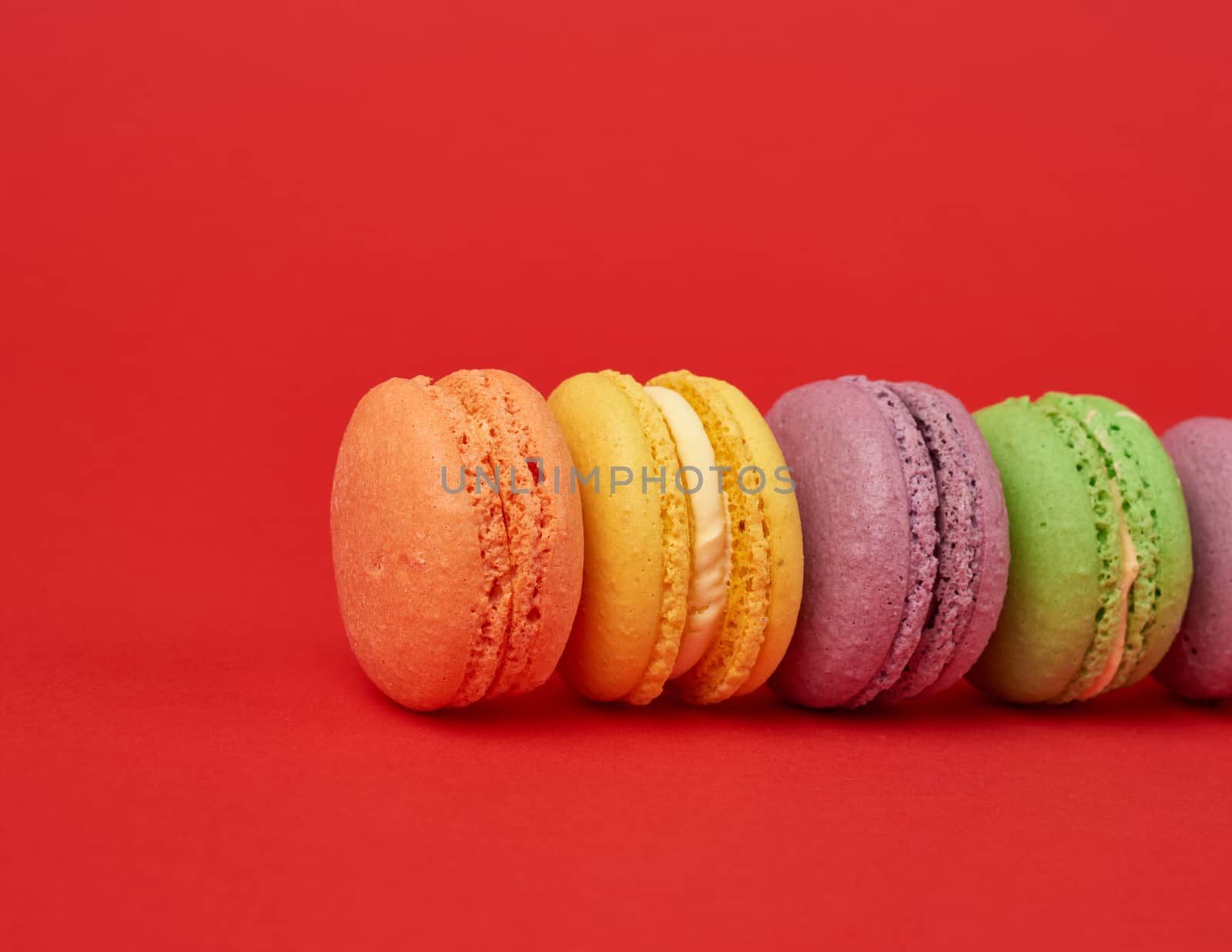 pile of multi-colored baked macarons almond flour cakes on a red background