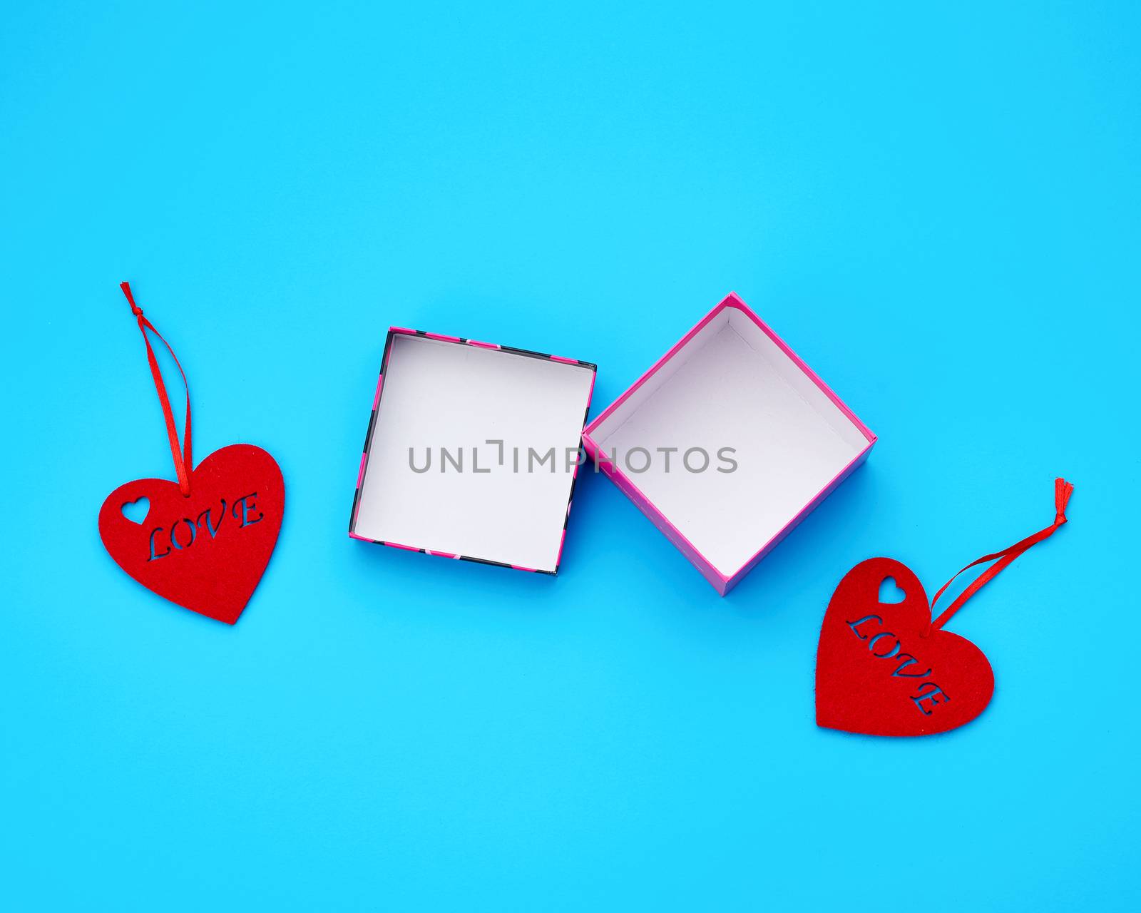 open cardboard square empty box and felt red hearts on a light blue background, top view