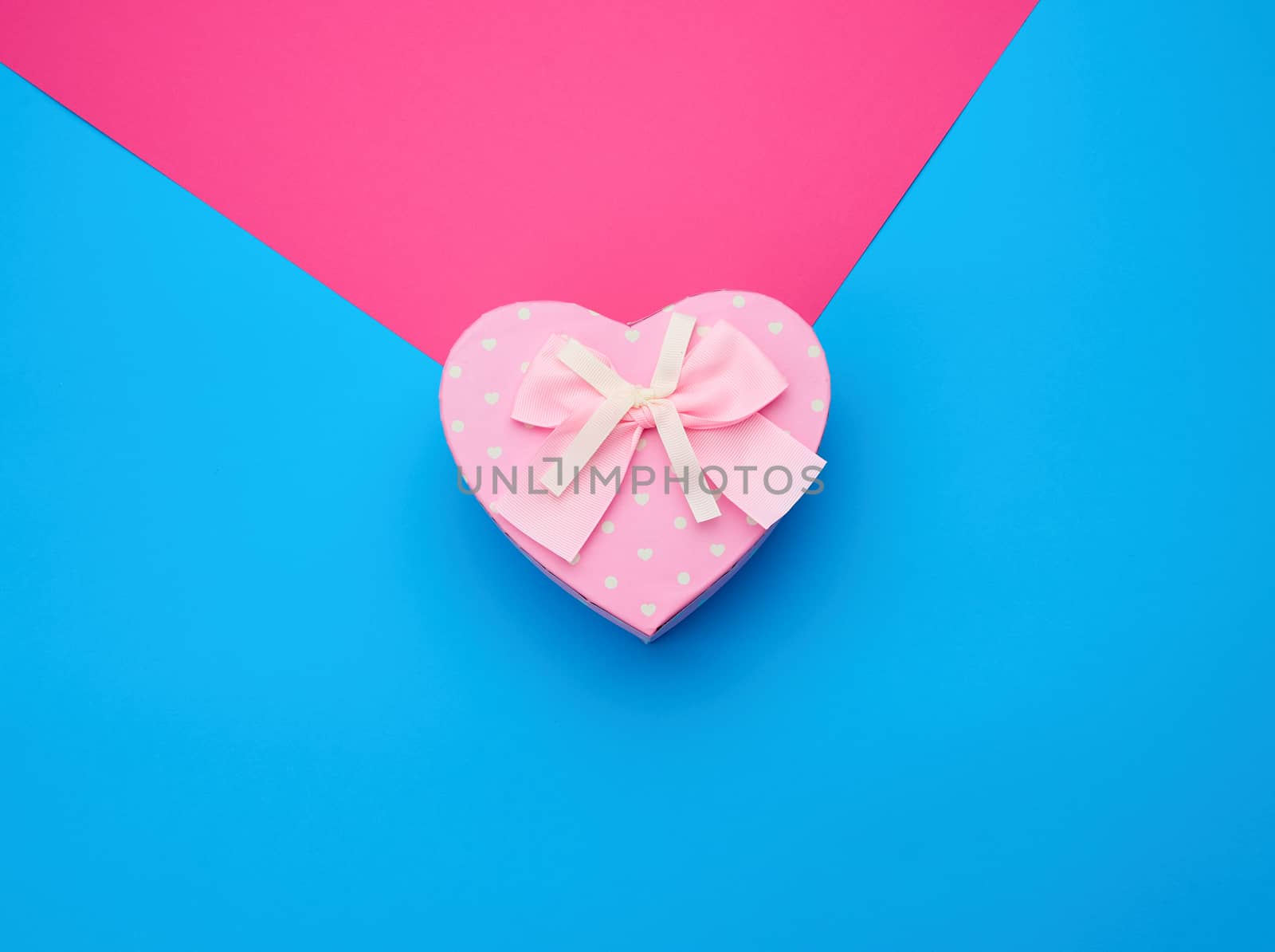pink gift box in the form of a heart with a bow on a blue background, top view, festive backdrop