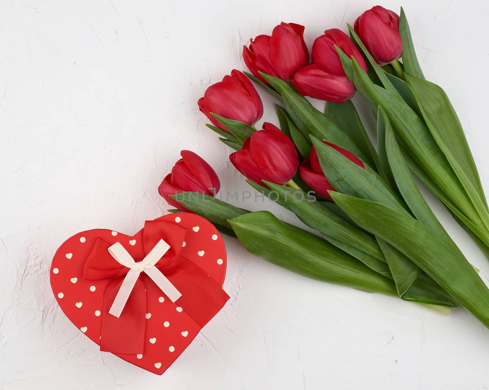 bouquet of red blooming tulips with green leaves, wrapped gift in brown craft paper on a white background, copy space. Festive backdrop for birthday, Valentine's day
