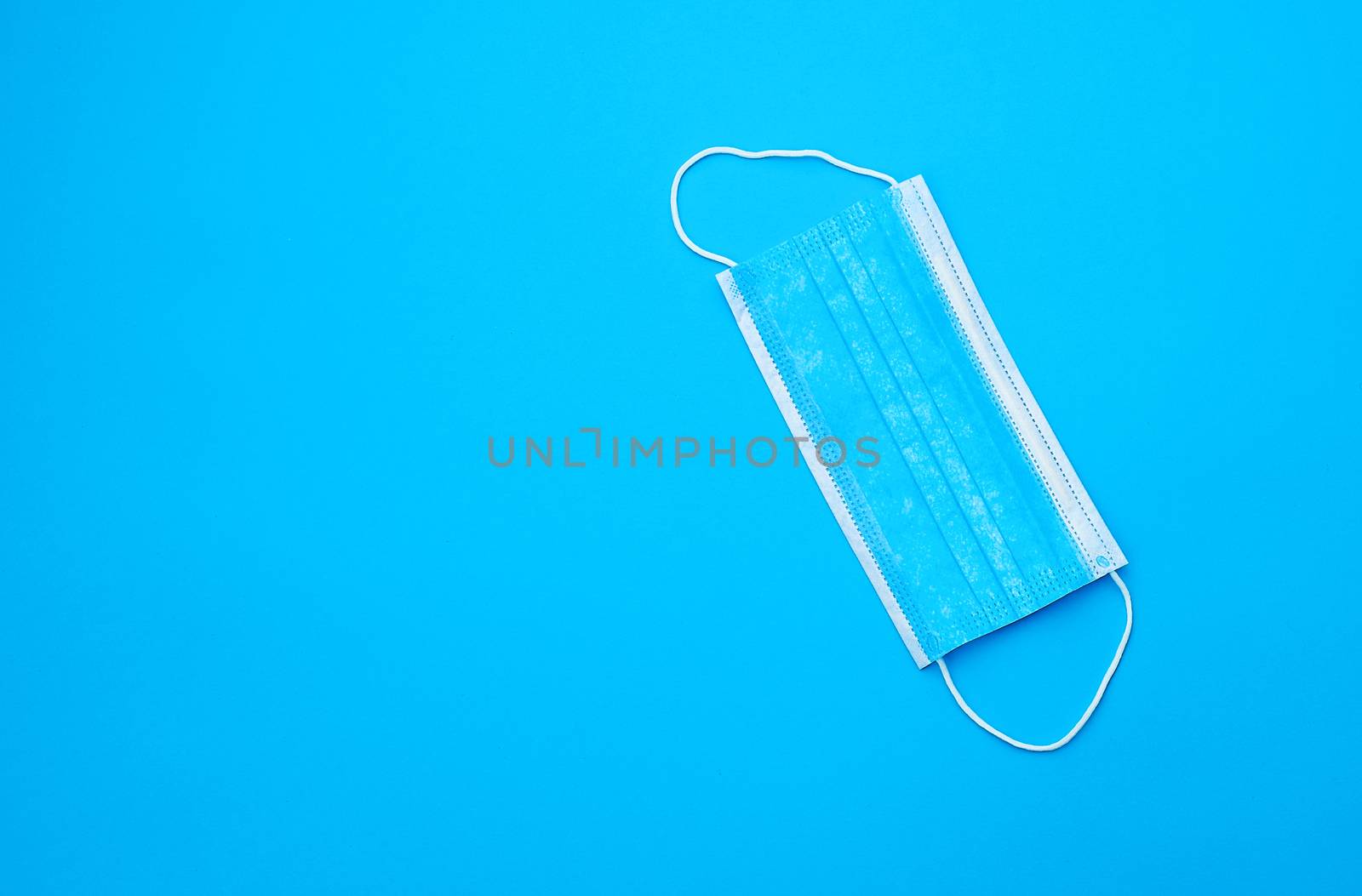 blue sterile medical mask with white elastic bands for doctors on a light blue background, flat lay, copy space