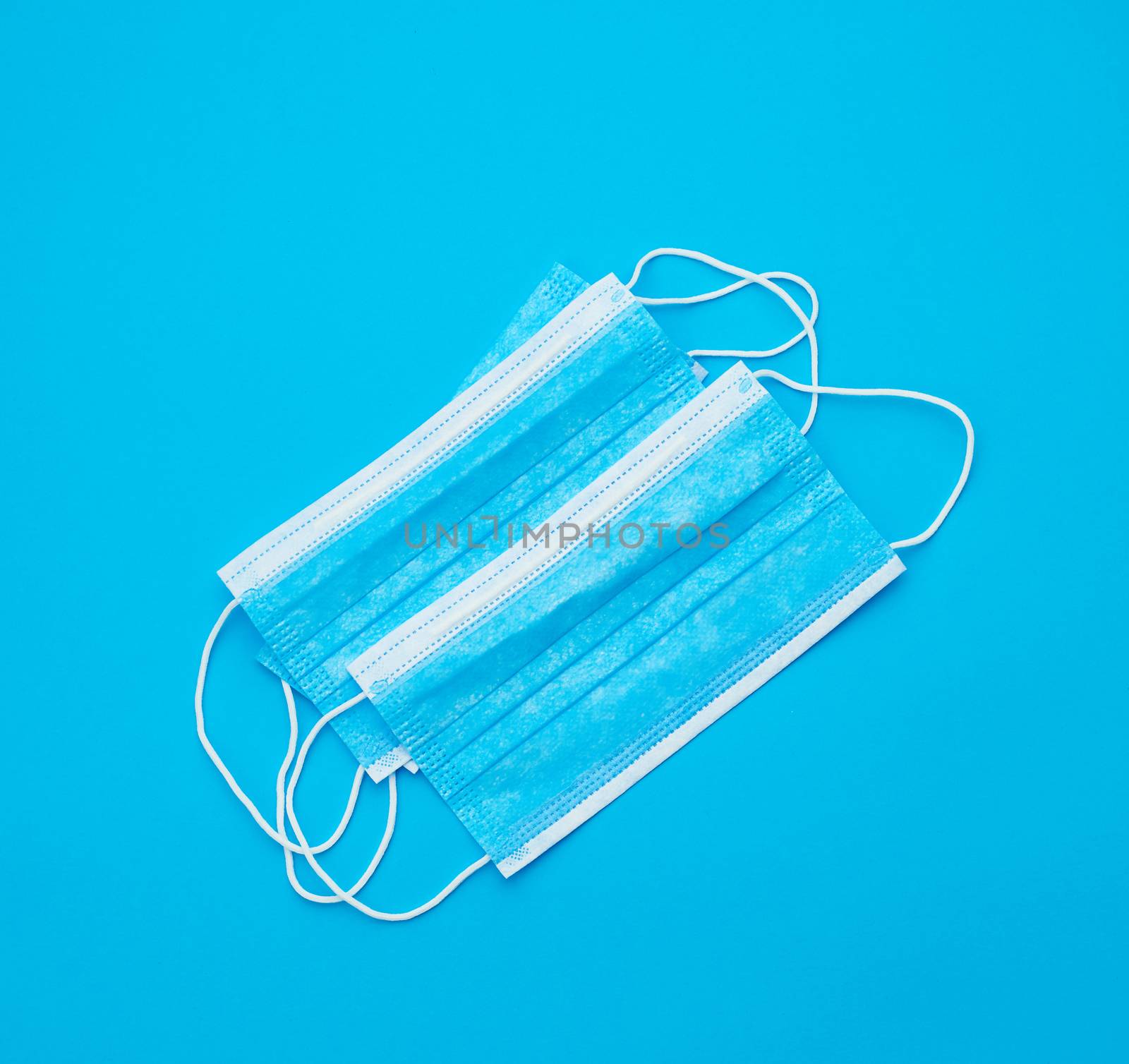 blue sterile medical mask with white elastic bands for doctors on a light blue background, flat lay