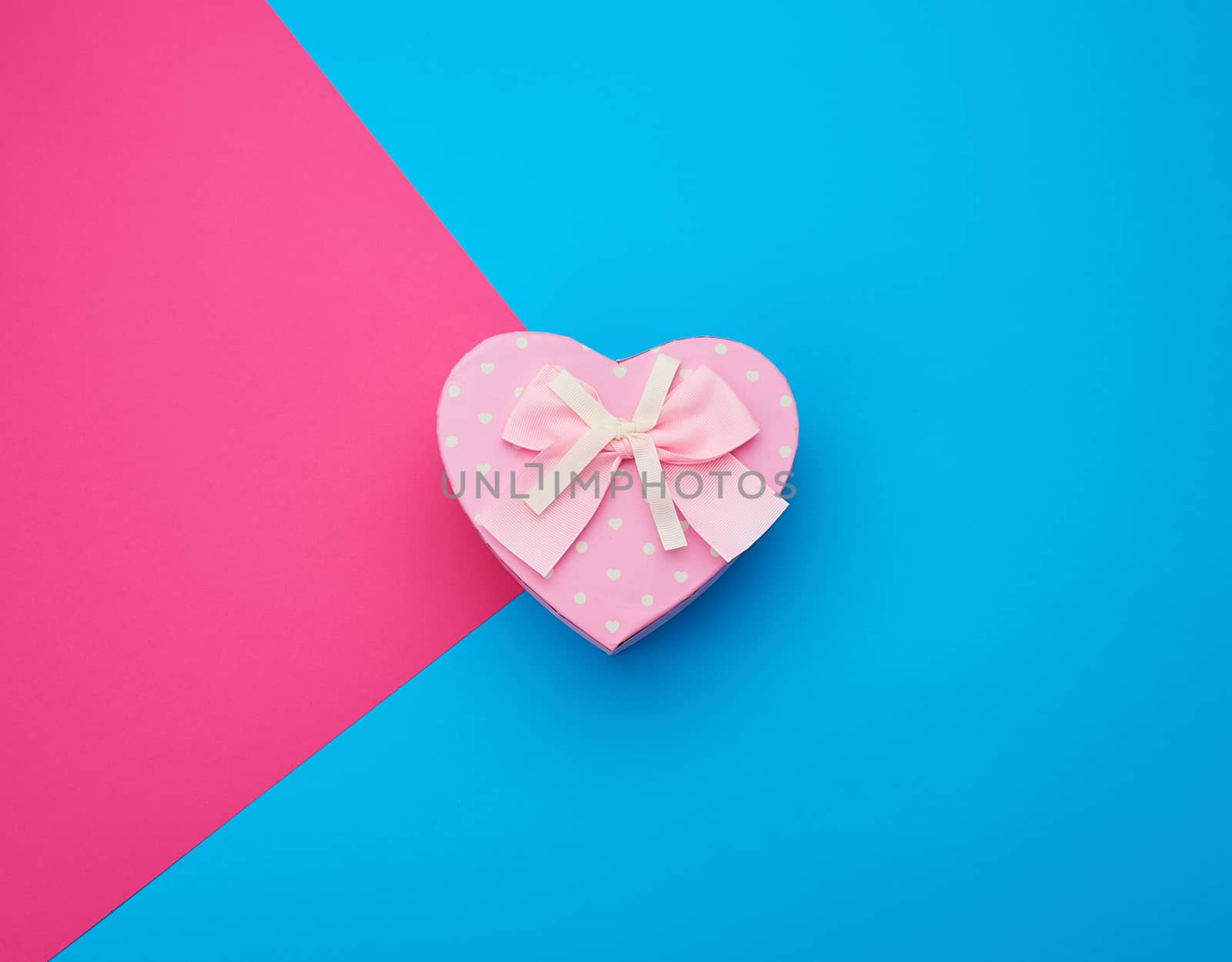 pink gift box in the form of a heart with a bow on a blue background, top view, festive backdrop