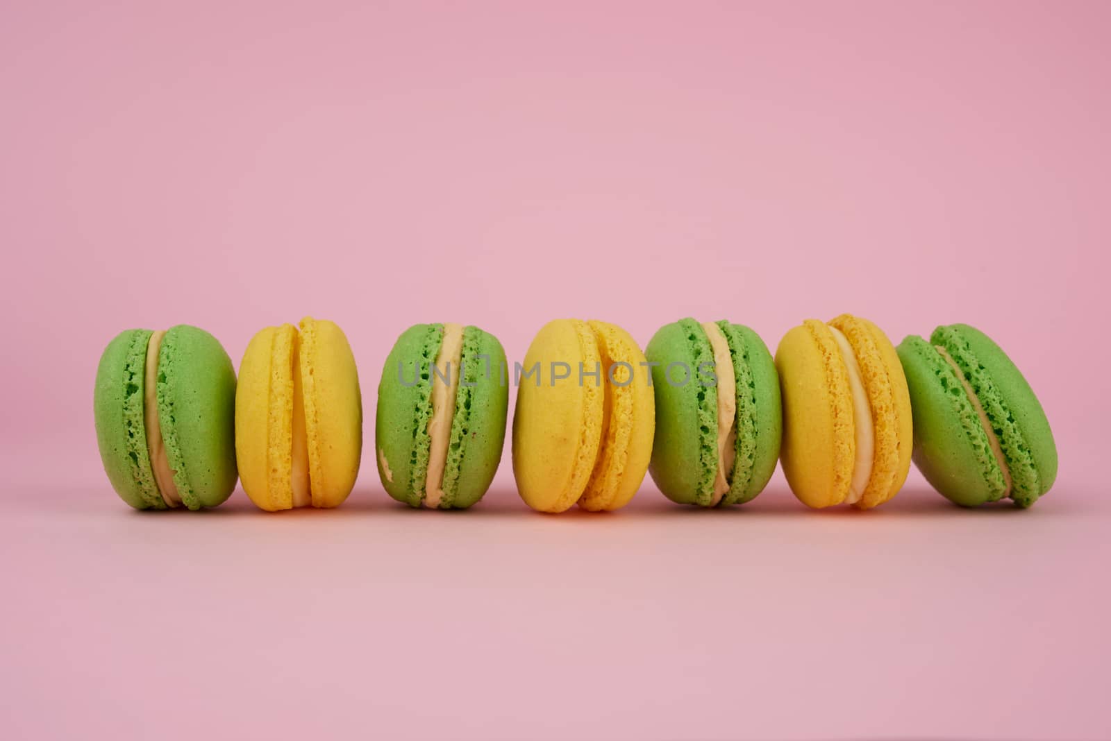 green and yellow round baked macarons on a pink background, delicious popular french dessert