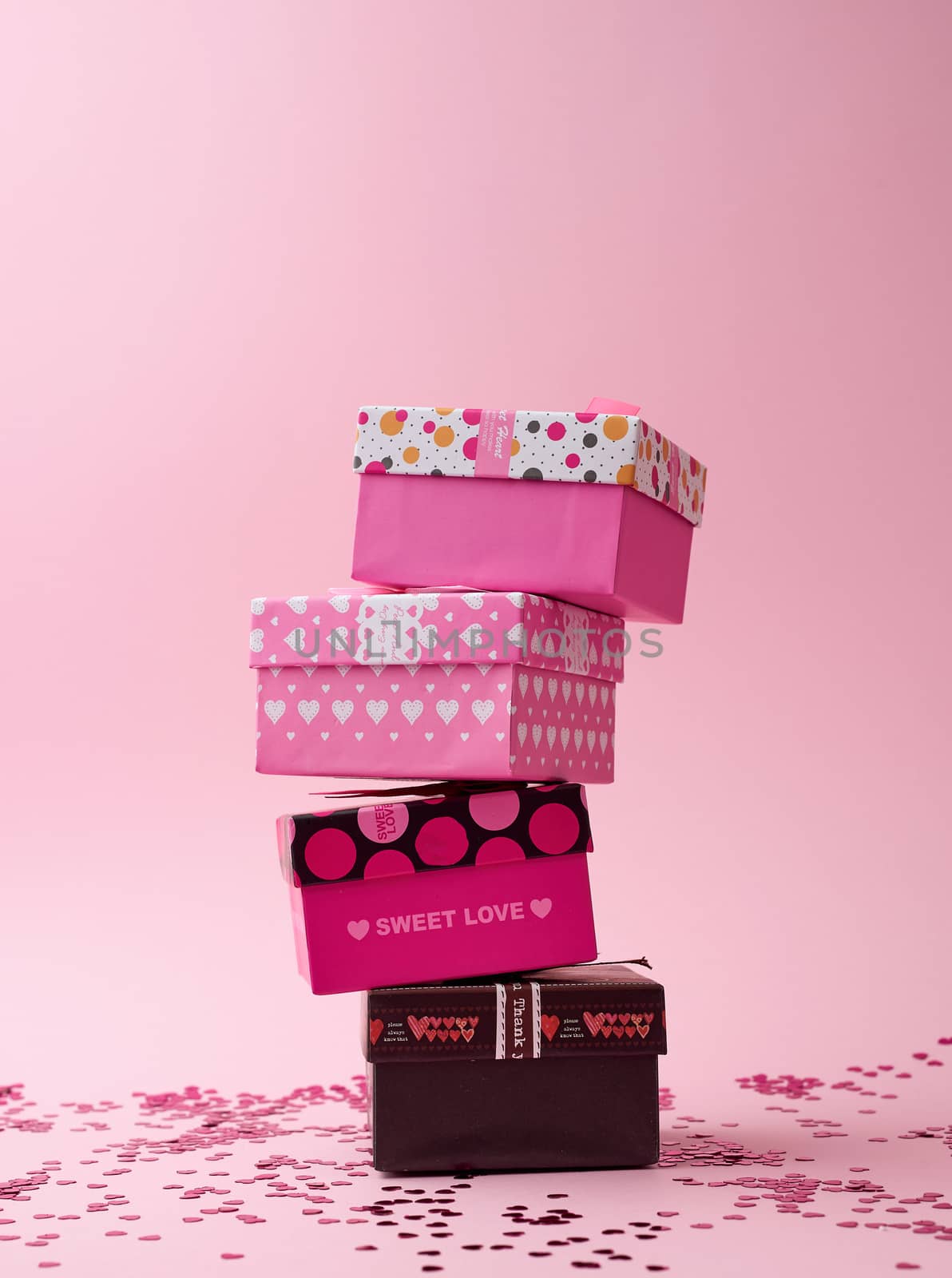 stack of cardboard square gift boxes on a pink background with shiny confetti, festive backdrop