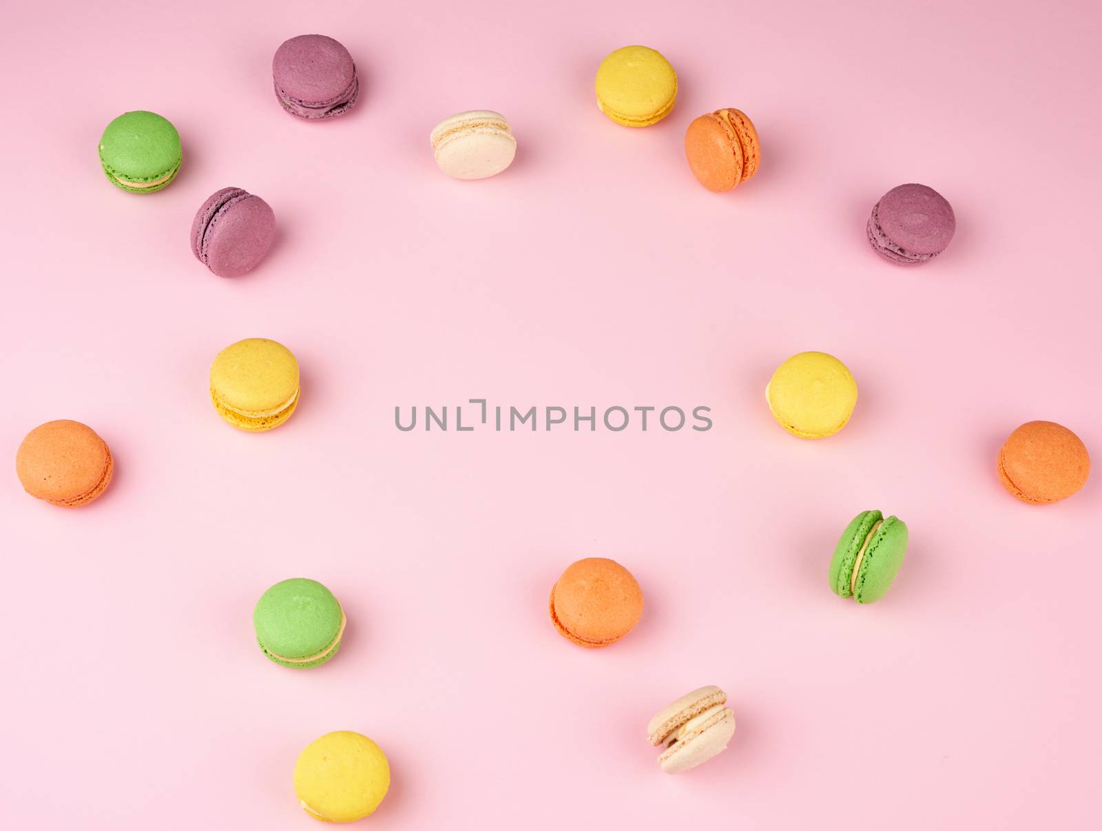 many multi-colored round baked macarons cakes on a light pink background, top view