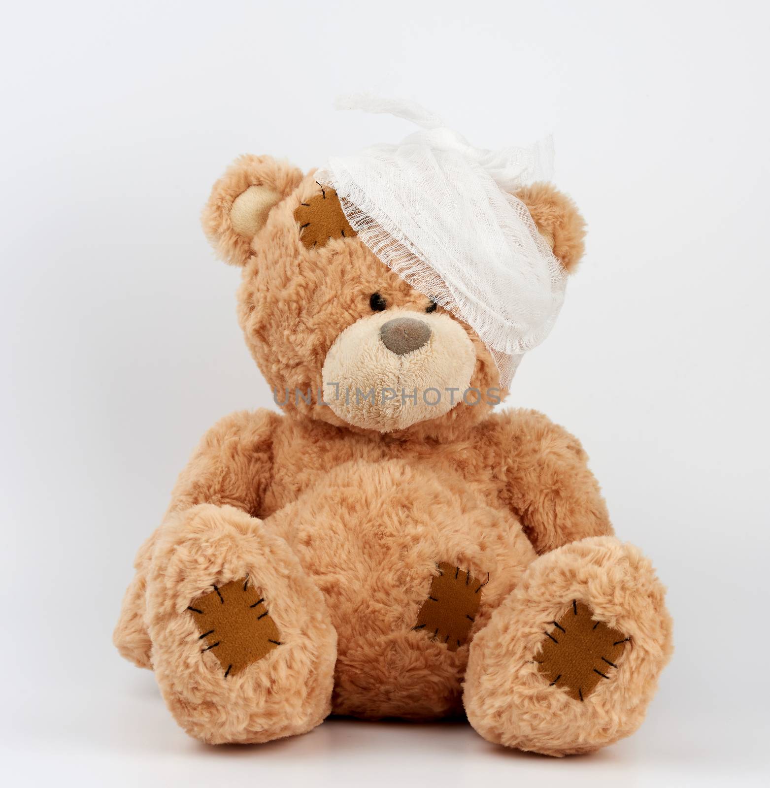 big teddy bear with a bandaged head in a white medical bandage on a white background, concept of child trauma, toy with patches
