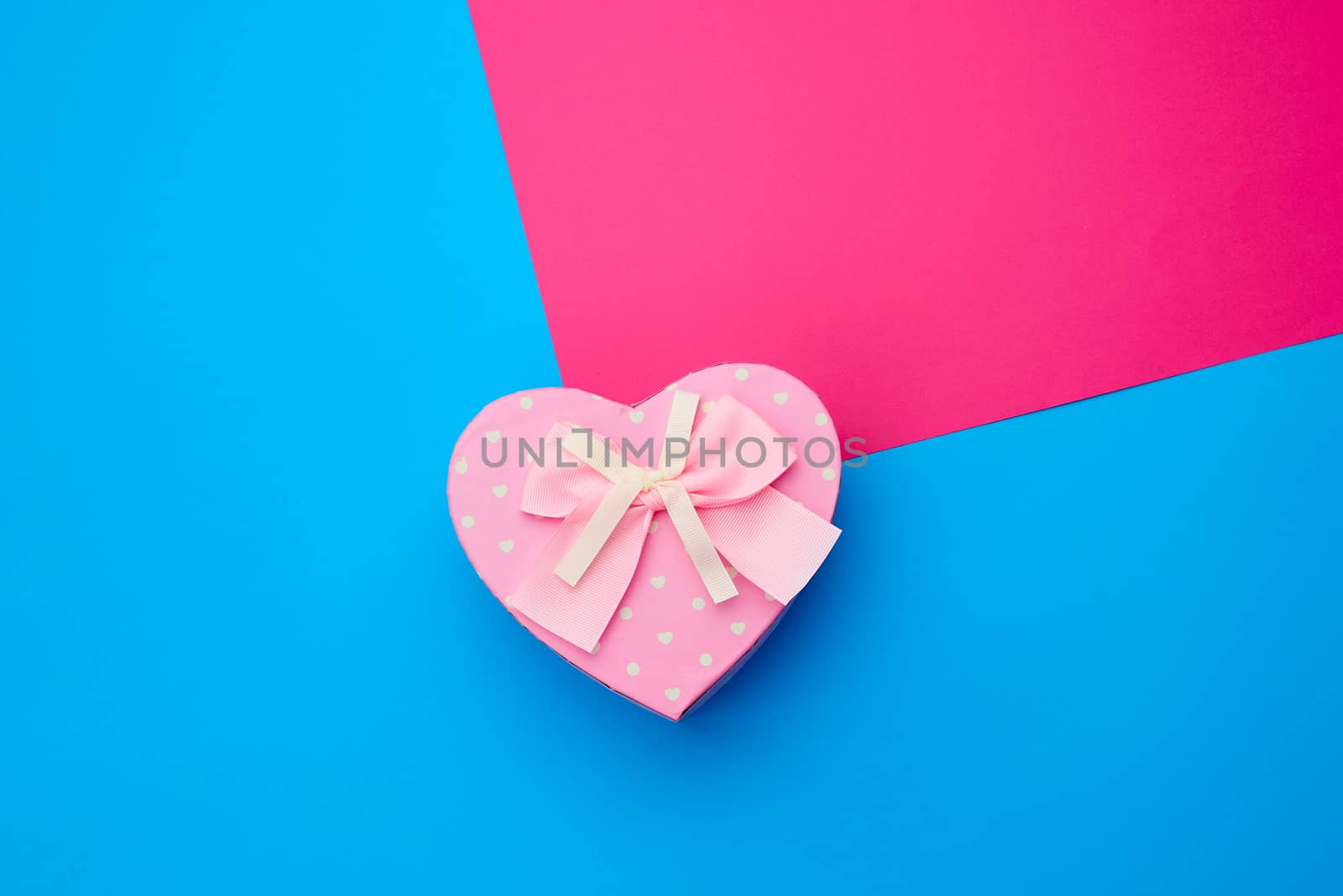 pink gift box in the form of a heart with a bow on a blue background, top view, festive backdrop