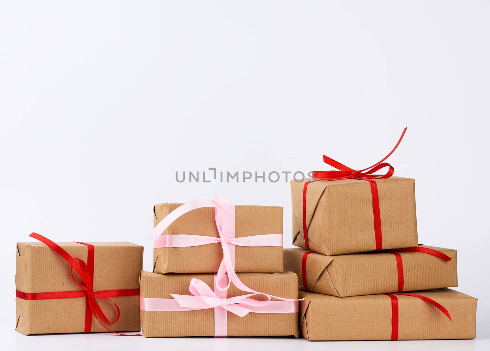 stack of gifts in boxes wrapped in brown kraft paper and tied with silk ribbon on a white background. Festive concept, copy space