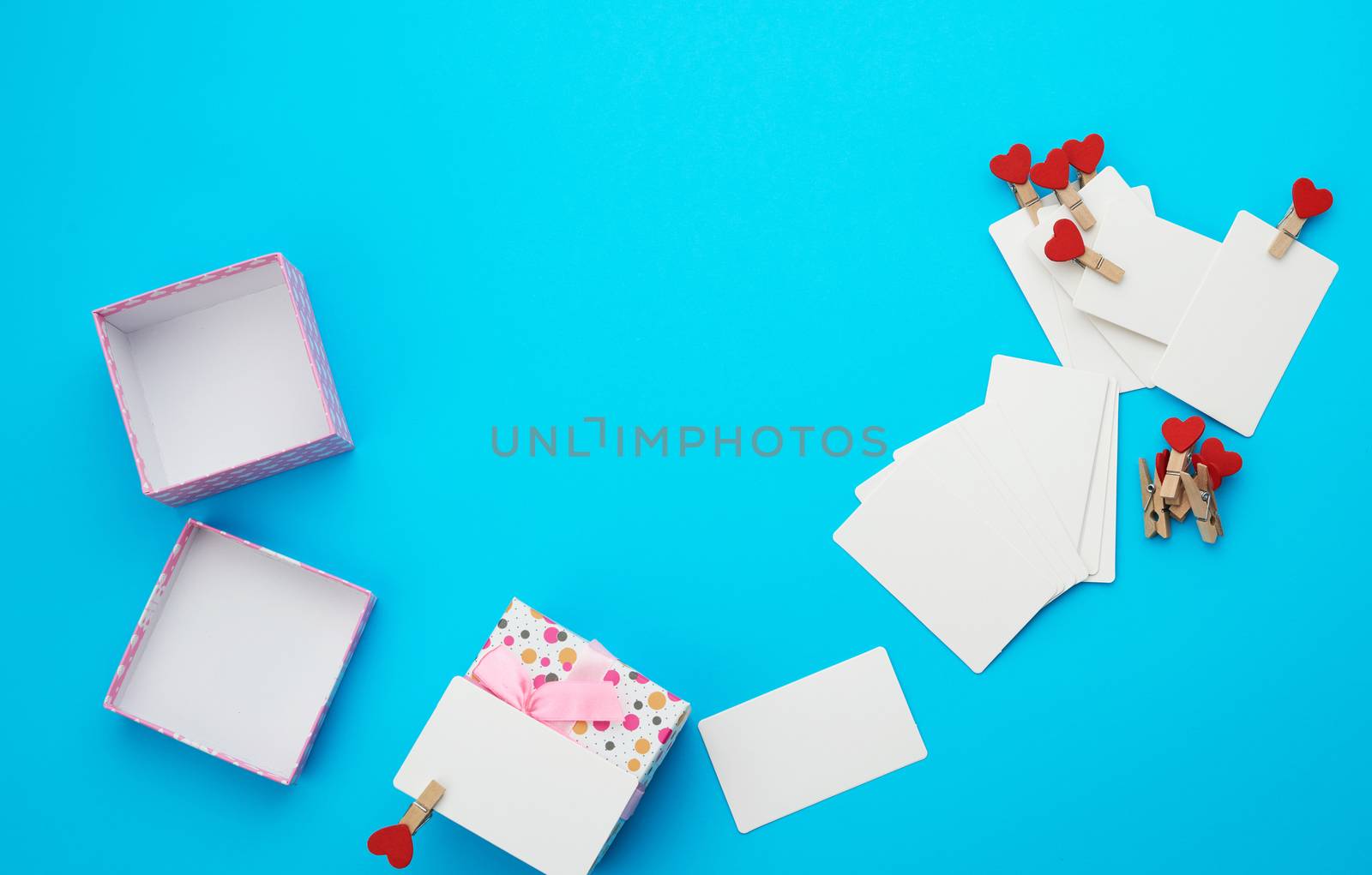 open square cardboard empty box and white blank paper rectangular business cards on decorative clothespins, item lies on a blue background, top view, copy space