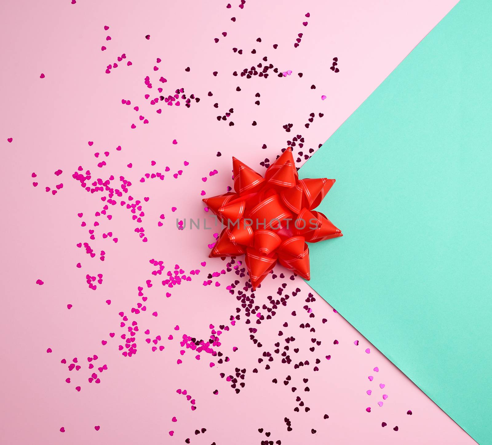 red bow and shiny multicolored round confetti scattered on a pink-green abstract background, festive backdrop for birthday, valentines day