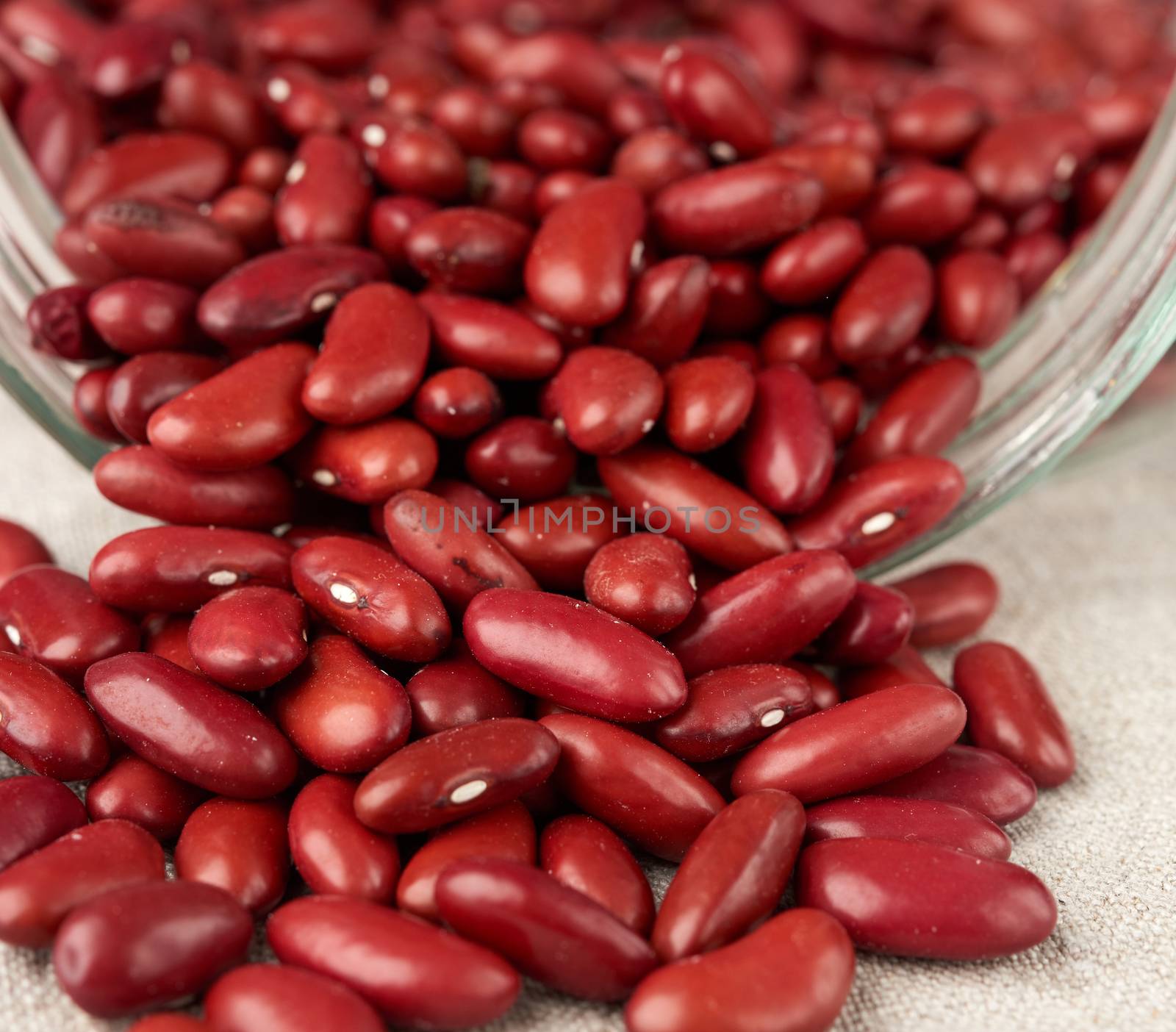 scattered red raw beans from a glass jar on a gray linen napkin, close up