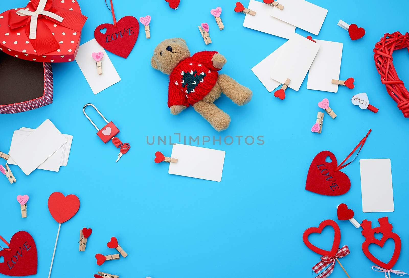 cardboard boxes in the form of a heart, a small teddy bear, white blank business cards with clothespins on a blue background, decor and objects for Valentine's Day, flat lay, copy space