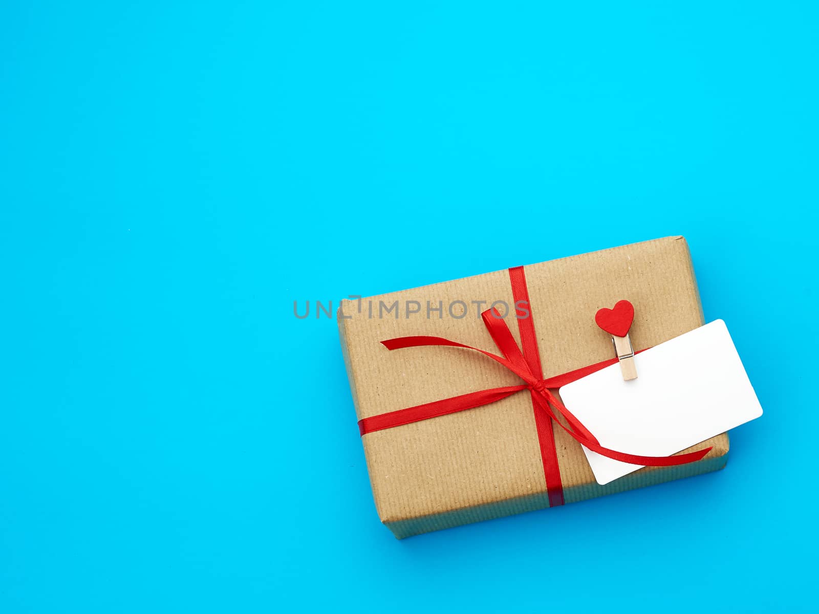 box is wrapped in brown paper and tied with a red thin silk ribbon on a blue background, copy space, holiday is Valentine's Day