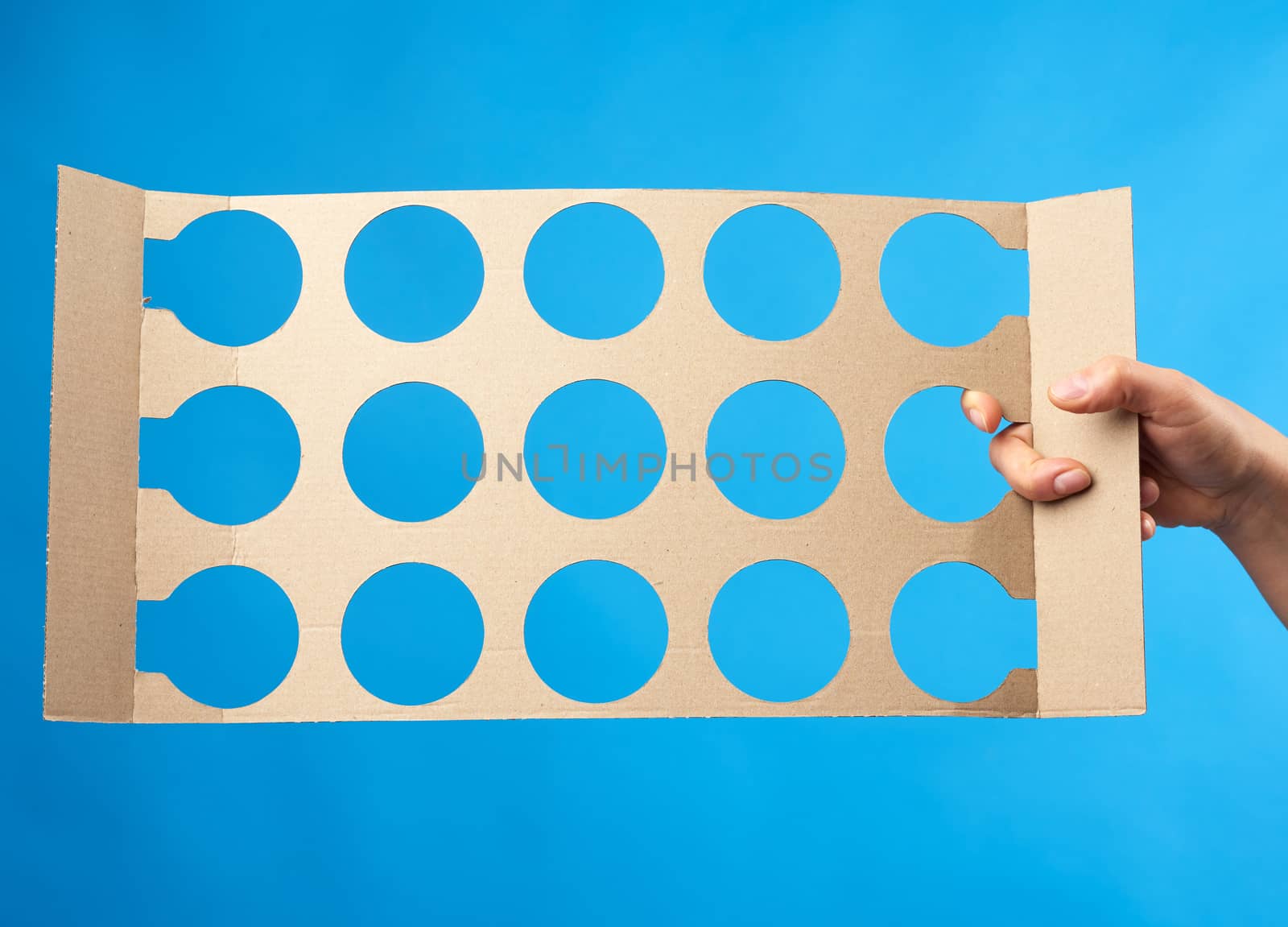 hand holds brown paper partition with round drawer openings, blue background 