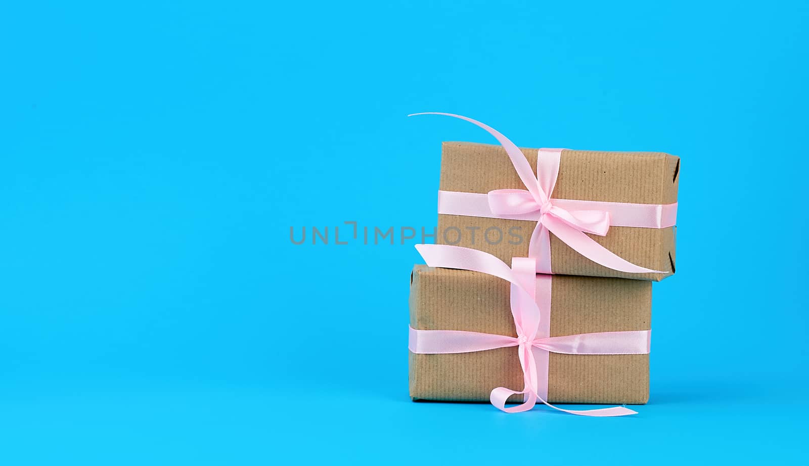 gifts in boxes wrapped in brown kraft paper and tied with pink silk ribbon on a blue background. Festive concept, copy space