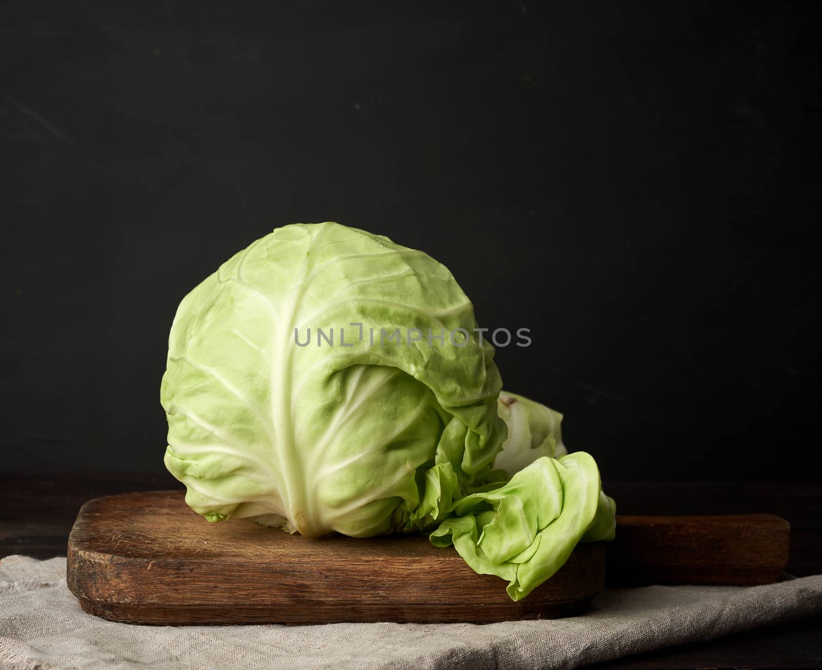 whole head of fresh green cabbage on a brown wooden board, wholesome food