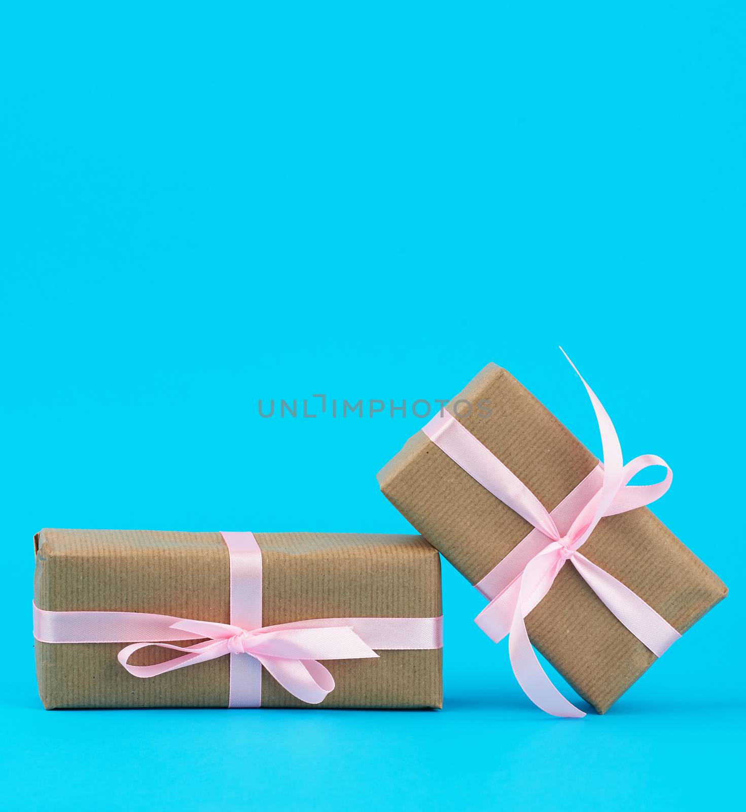  gifts in boxes wrapped in brown kraft paper and tied with pink silk ribbon on a blue background. Festive concept, copy space