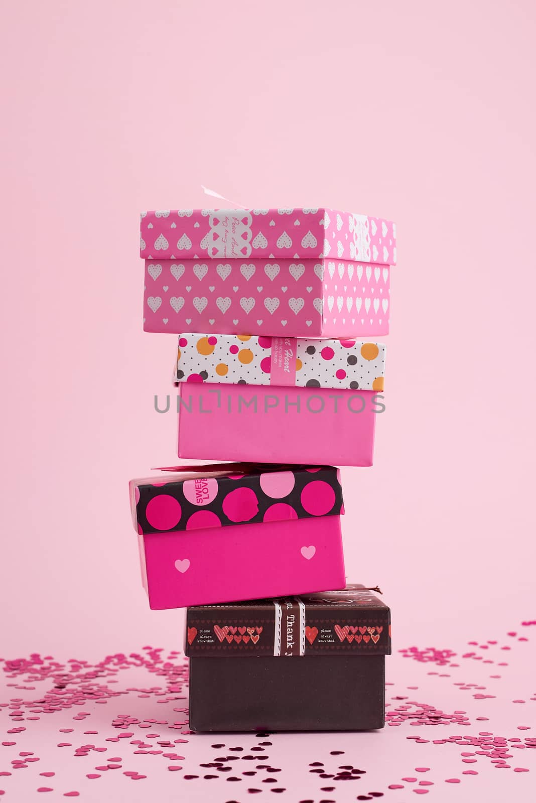 stack of cardboard square gift boxes on a pink background with shiny confetti, festive backdrop