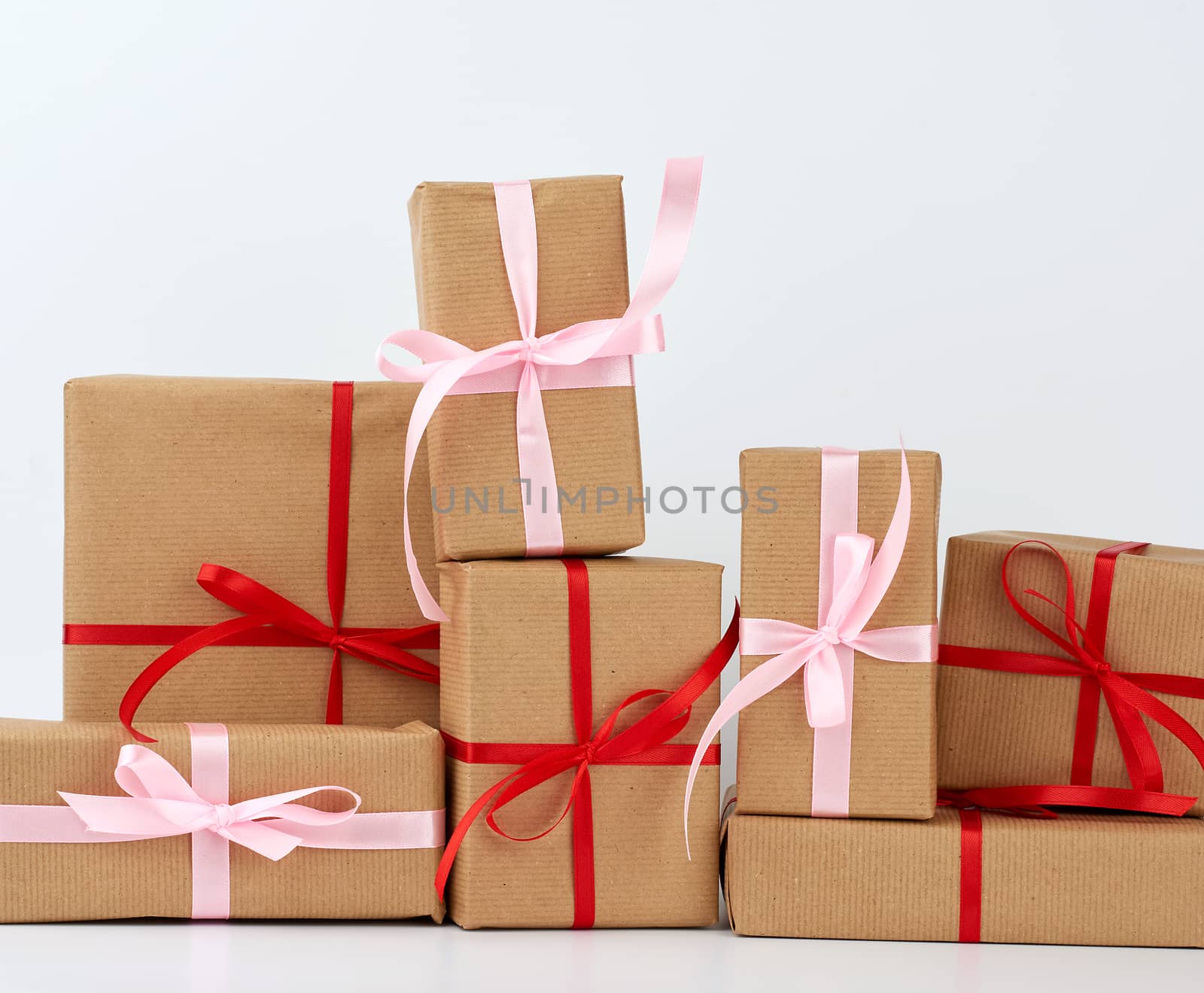 stack of gifts in boxes wrapped in brown kraft paper and tied with silk ribbon on a white background. Festive concept, copy space