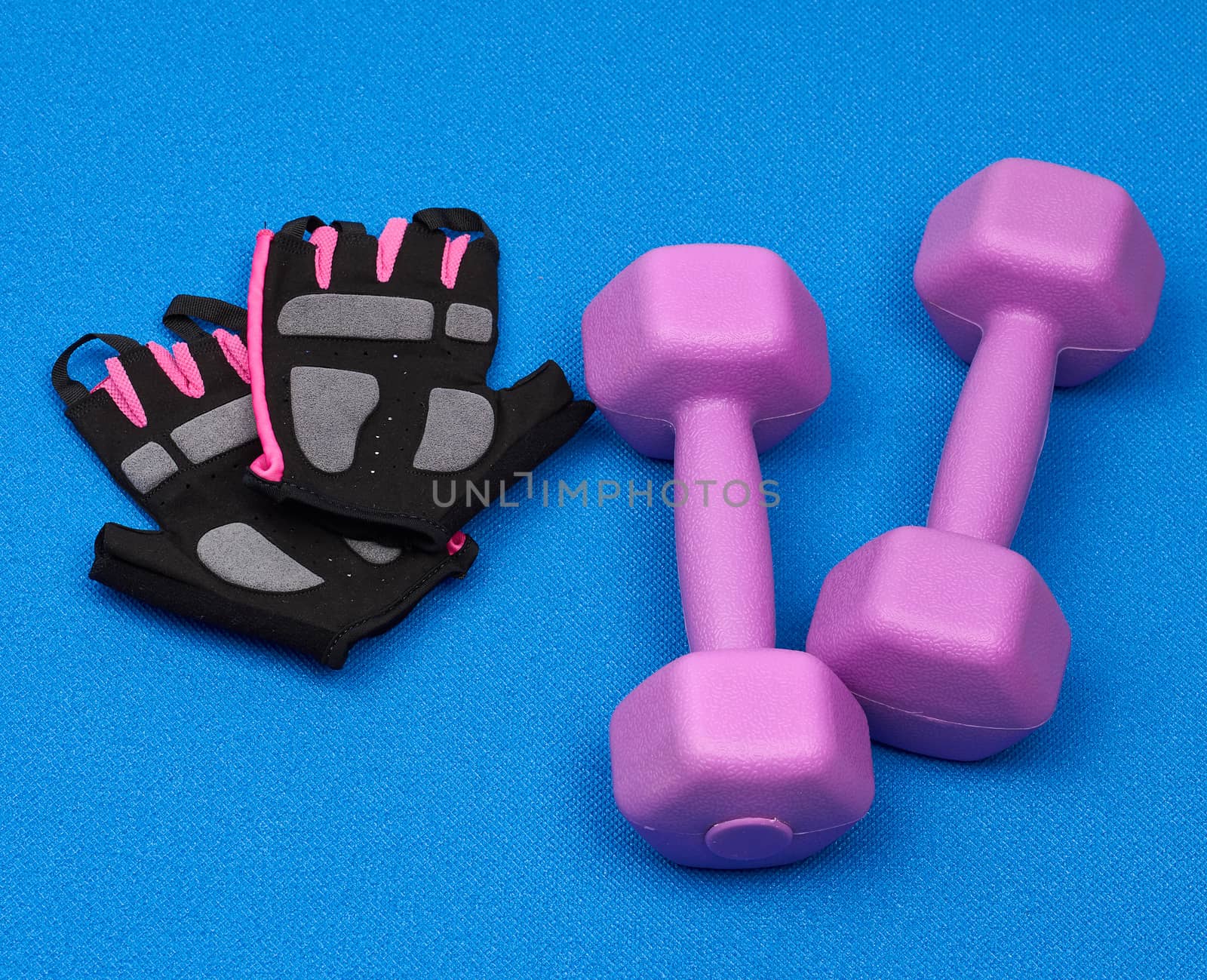 pair of purple plastic dumbbells, gloves on a blue neoprene mat, top view, training equipment