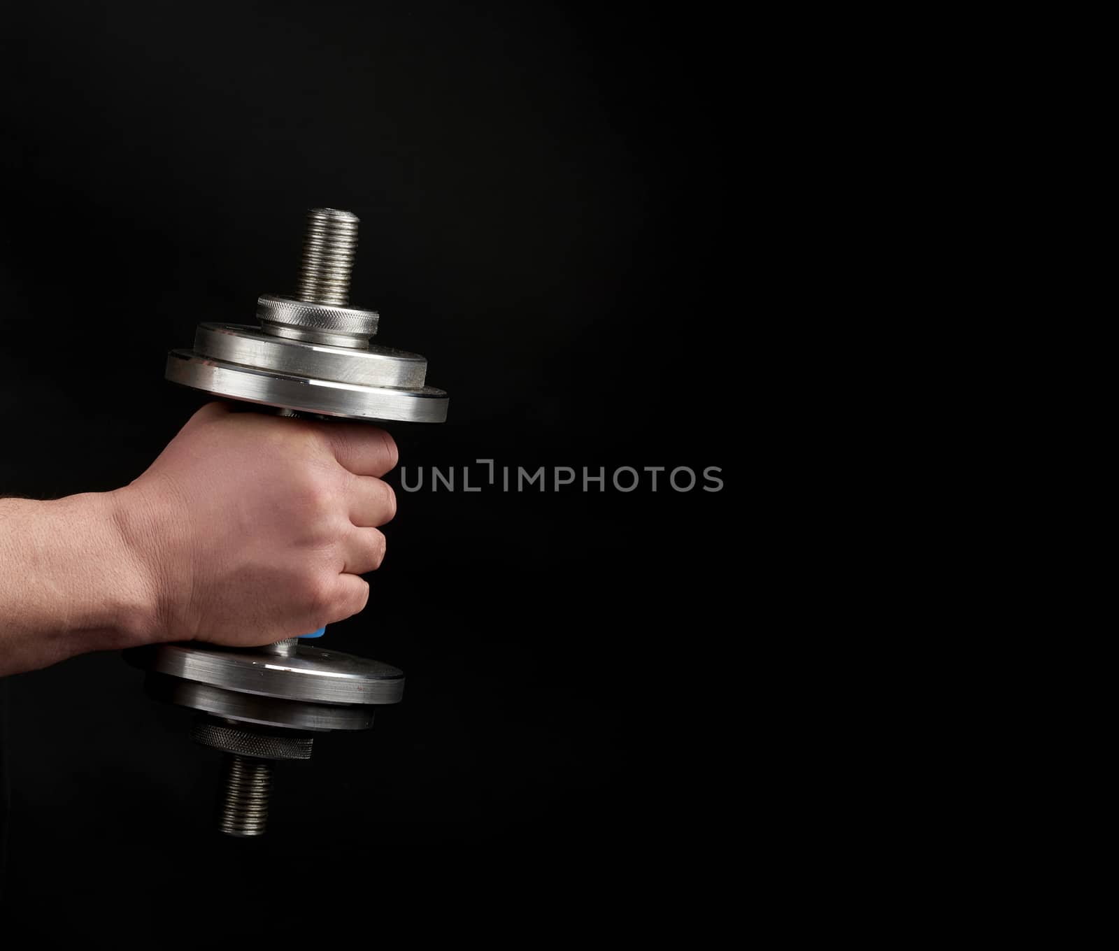 man holds steel dumbbells in his hands, his muscles are tense, low key, sports background, copy space