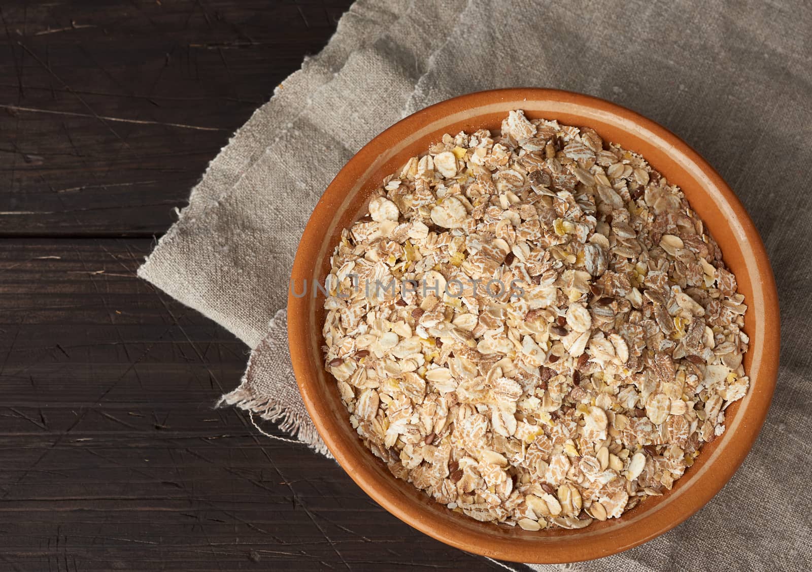 raw oatmeal in a brown ceramic plate on a wooden table, top view