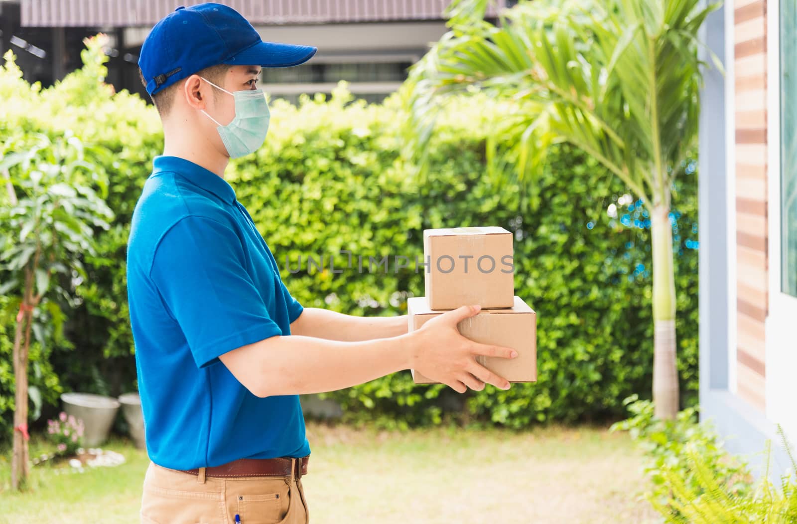 Asian delivery express courier young man use giving boxes to woman customer he wearing protective face mask at front home, under curfew quarantine pandemic coronavirus COVID-19