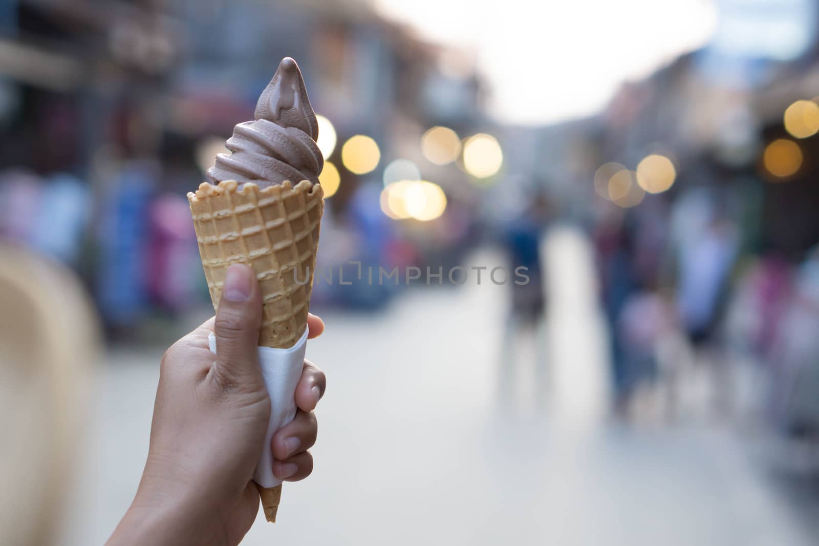 Closeup woman hand holding chocolate ice cream on walking street, selective focus
