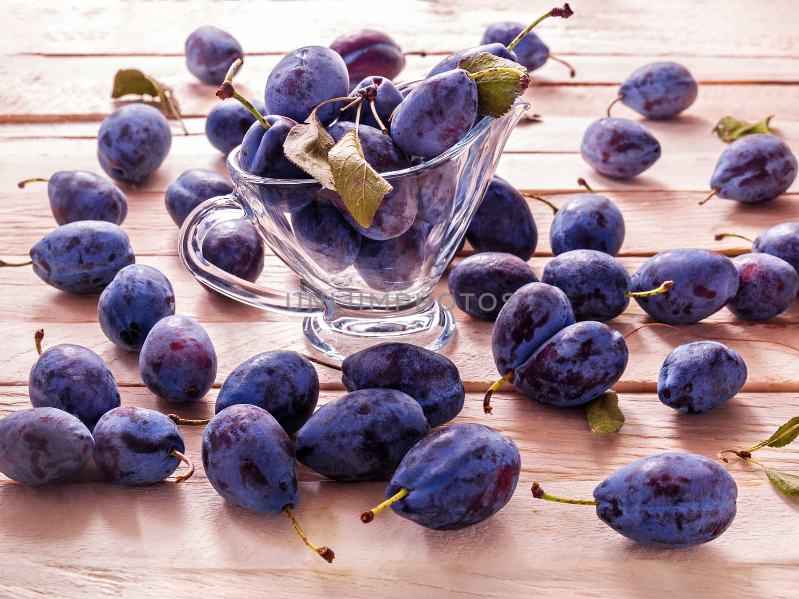 Blue large plums juicy sweet fruit for dietary nutrition lie in a glass goblet on a plank background