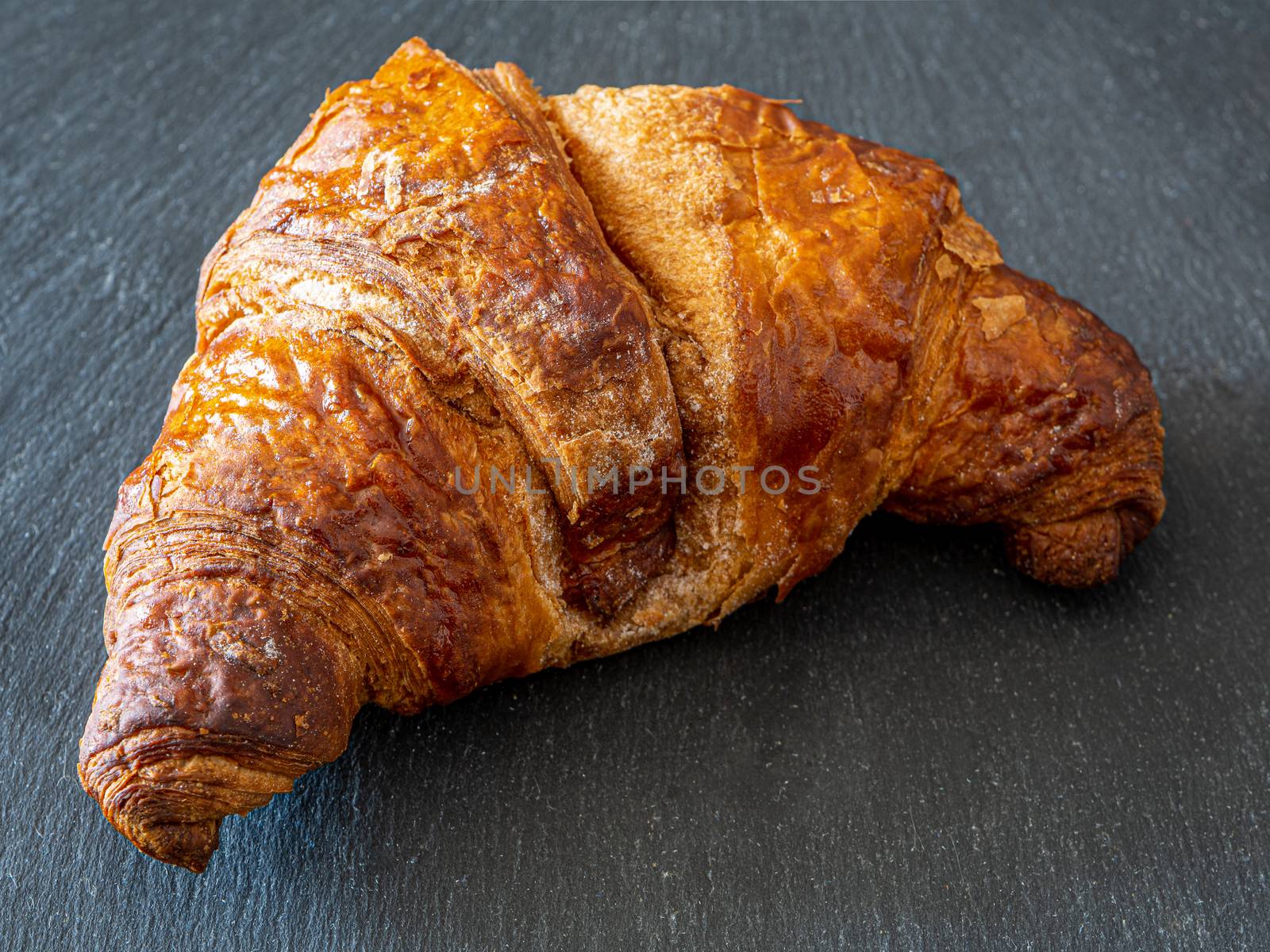 Traditional croissant placed on a dark plate, a typical dessert similar to the Italian Cornetto
