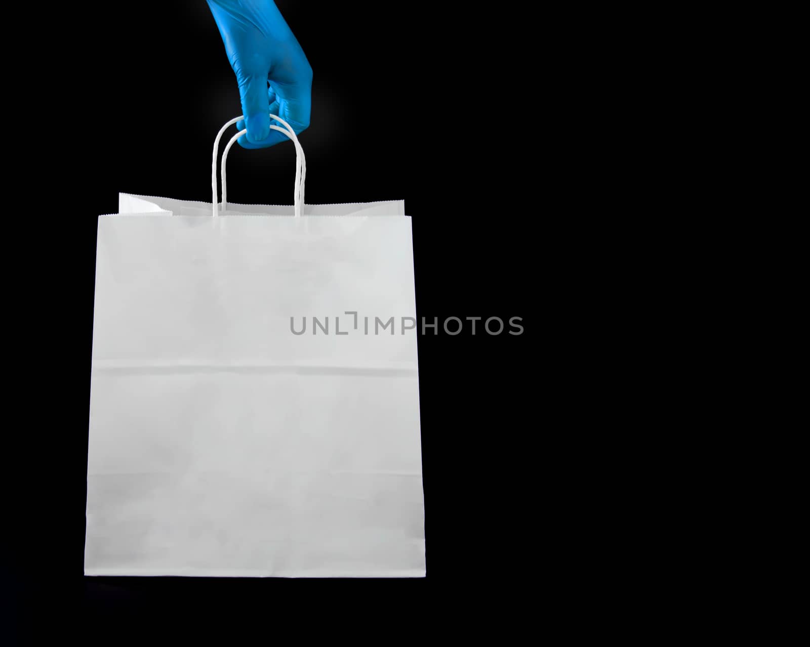A person wearing protective latex gloves holding a shopping paper bag
